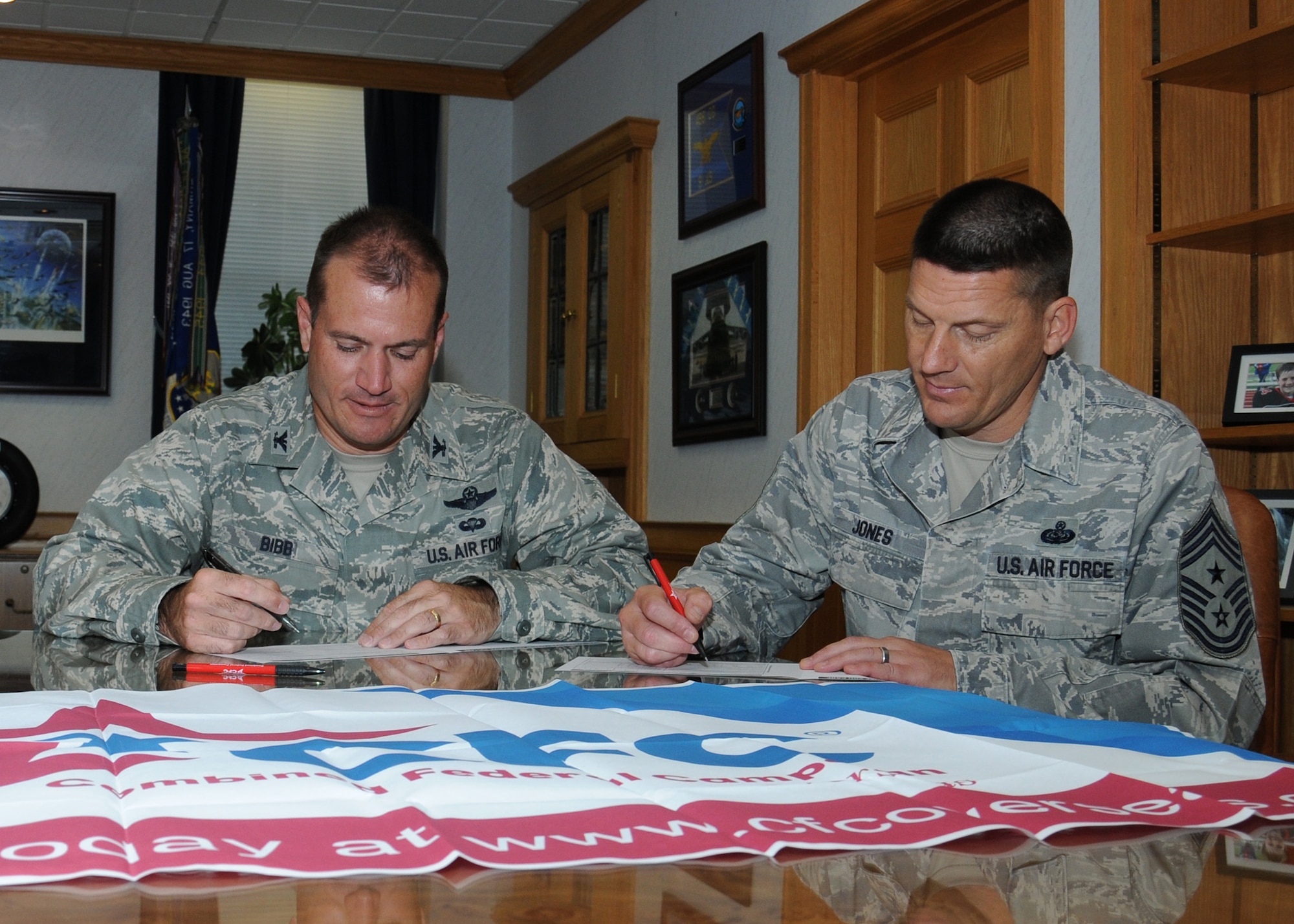 U.S. Air Force Col. Kenneth T. Bibb Jr., left, 100th Air Refueling Wing commander, and U.S. Air Force Chief Master Sgt. Tracy Jones, 100th ARW command chief, sign Combined Federal Campaign donation forms in Bibb’s office Sept. 4, 2013, on RAF Mildenhall, England. The campaign will run from Sept. 16 through Nov. 15, 2013. Participants are able to donate to a charity of their choice, including Family Support and Youth Programs — funds that go directly back to Team Mildenhall members. (U.S. Air Force photo by Gina Randall/Released)