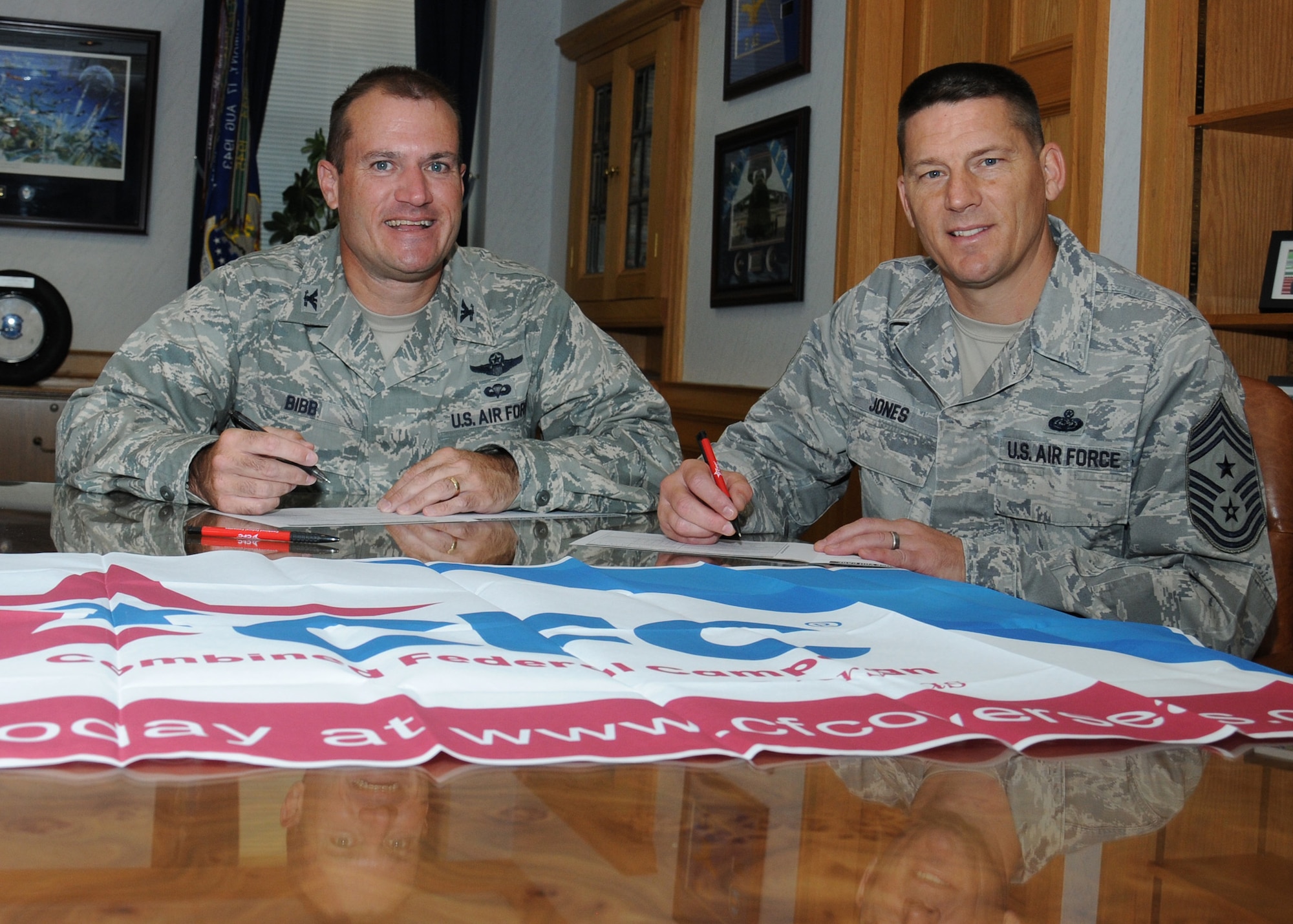 U.S. Air Force Col. Kenneth T. Bibb Jr., left, 100th Air Refueling Wing commander, and U.S. Air Force Chief Master Sgt. Tracy Jones, 100th ARW command chief, prepare to sign Combined Federal Campaign donation forms in Bibb’s office Sept. 4, 2013, on RAF Mildenhall, England. The CFC is a voluntary program that provides federal employees the opportunity to donate to charities through payroll deductions or a one-time payment. (U.S. Air Force photo by Gina Randall/Released)