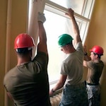 Senior Airman Jarrett Smith, center, works alongside Latvian soldiers installing new windows to the Ernst Gluck High school.