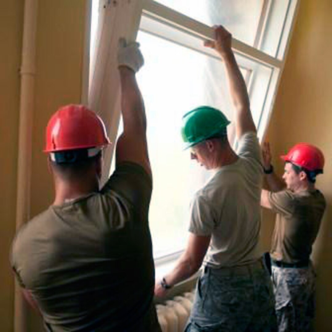 Senior Airman Jarrett Smith, center, works alongside Latvian soldiers installing new windows to the Ernst Gluck High school.