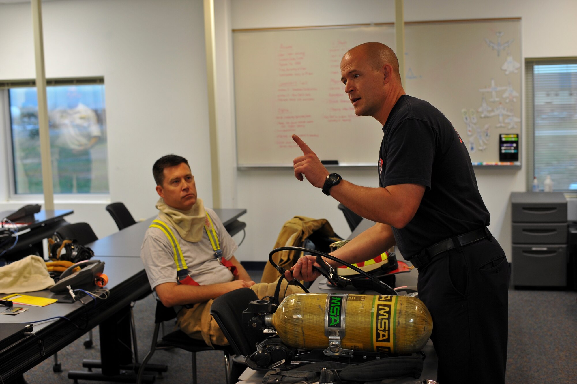 Jason Debord, Buckley firefighter, left, demonstrates the use of an air tank while Col. Dan Wright, 460th Space Wing commander, listens Sept. 5, 2013, at the Buckley Fire Department on Buckley Air Force Base, Colo. Wright, as well as Chief Master Sgt. Craig S. Hall, 460th SW command chief, and Lt. Col. Allen Thibeaux, 460th Civil Engineer Squadron commander, were brought through a fire immersion scenario designed to teach them the challenges firefighters face during an emergency.  (U.S. Air Force photo by Senior Airman Phillip Houk/Released)
