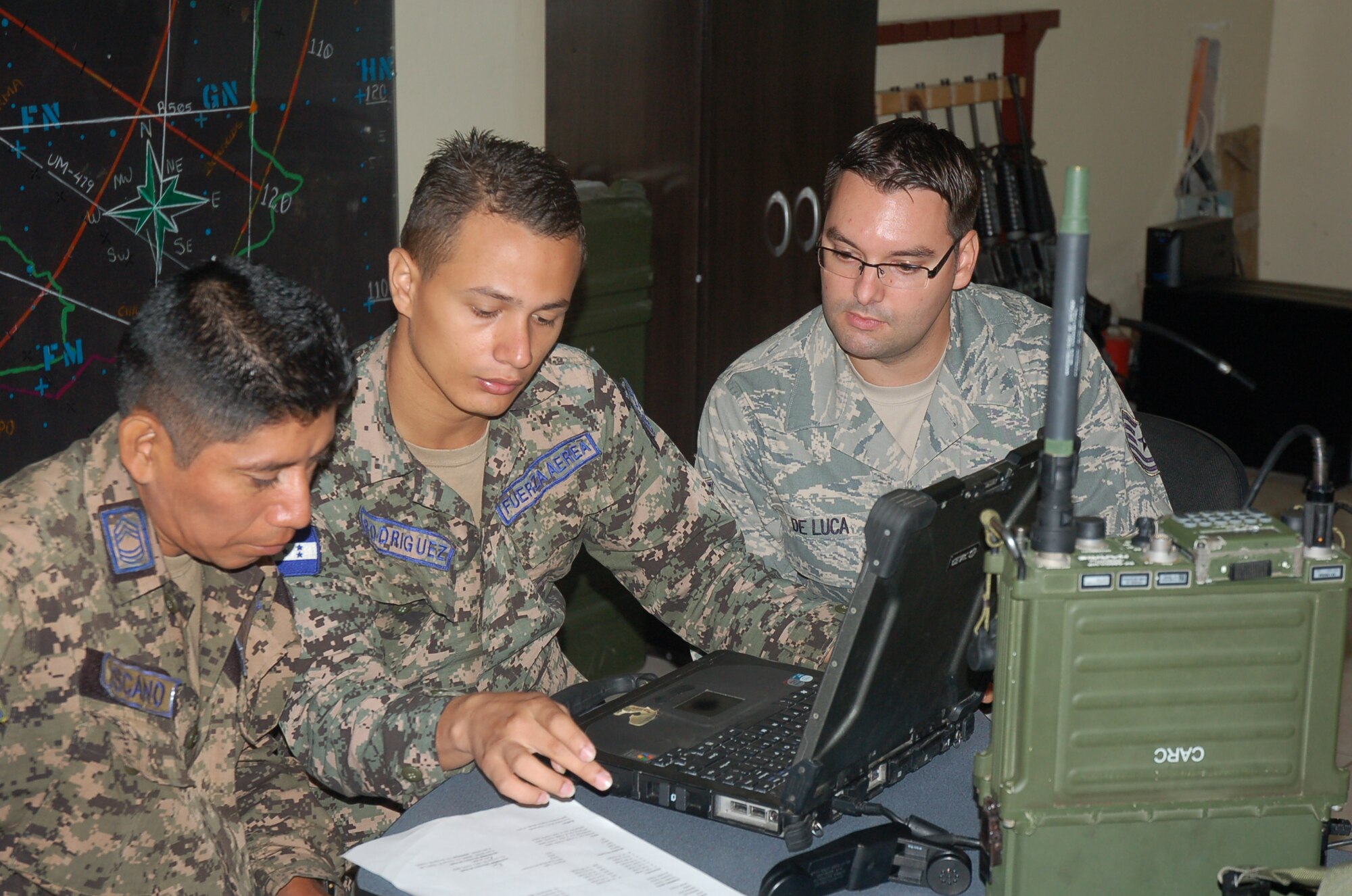 Tech. Sgt. Brian De Luca, 571st Mobility Support Advisory Squadron communications air advisor, observes the programming of a Harris RF-5800H-MP radio for secure communications between the Honduran Air Force and Navy during the MSAS building partner capacity engagement, 29 Jul – 24 Aug, at Base Aerea Hector Acosta Mejia, Tegucigalpa, Honduras. (U.S. Air Force photo by Tech. Sgt. Edgar Gonzalez)
