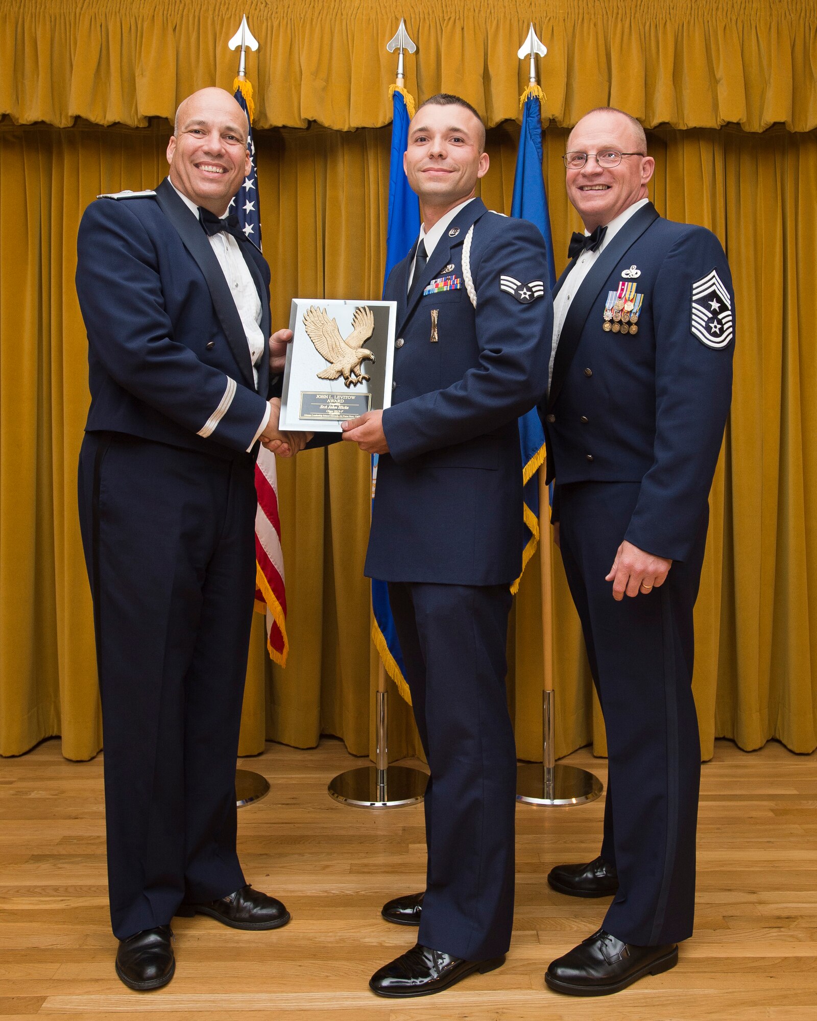 Senior Airman John Hicks, 412th Security Forces Squadron (center), is presented with with the John L. Levitow Award by Brig. Gen. Michael T. Brewer, 412th Test Wing commander (left), and Chief Master Sgt. Brian Randolph, 412th TW command chief, during an Airman Leadership School graduation Sept. 5 at Club Muroc. The award is given to the class's top graduate and is named after Vietnam War Medal of Honor awardee Sergeant John L. Levitow. ALS Class 13-F graduated 25 future noncommissioned officers. (U.S. Air Force photo by Ethan Wagner)