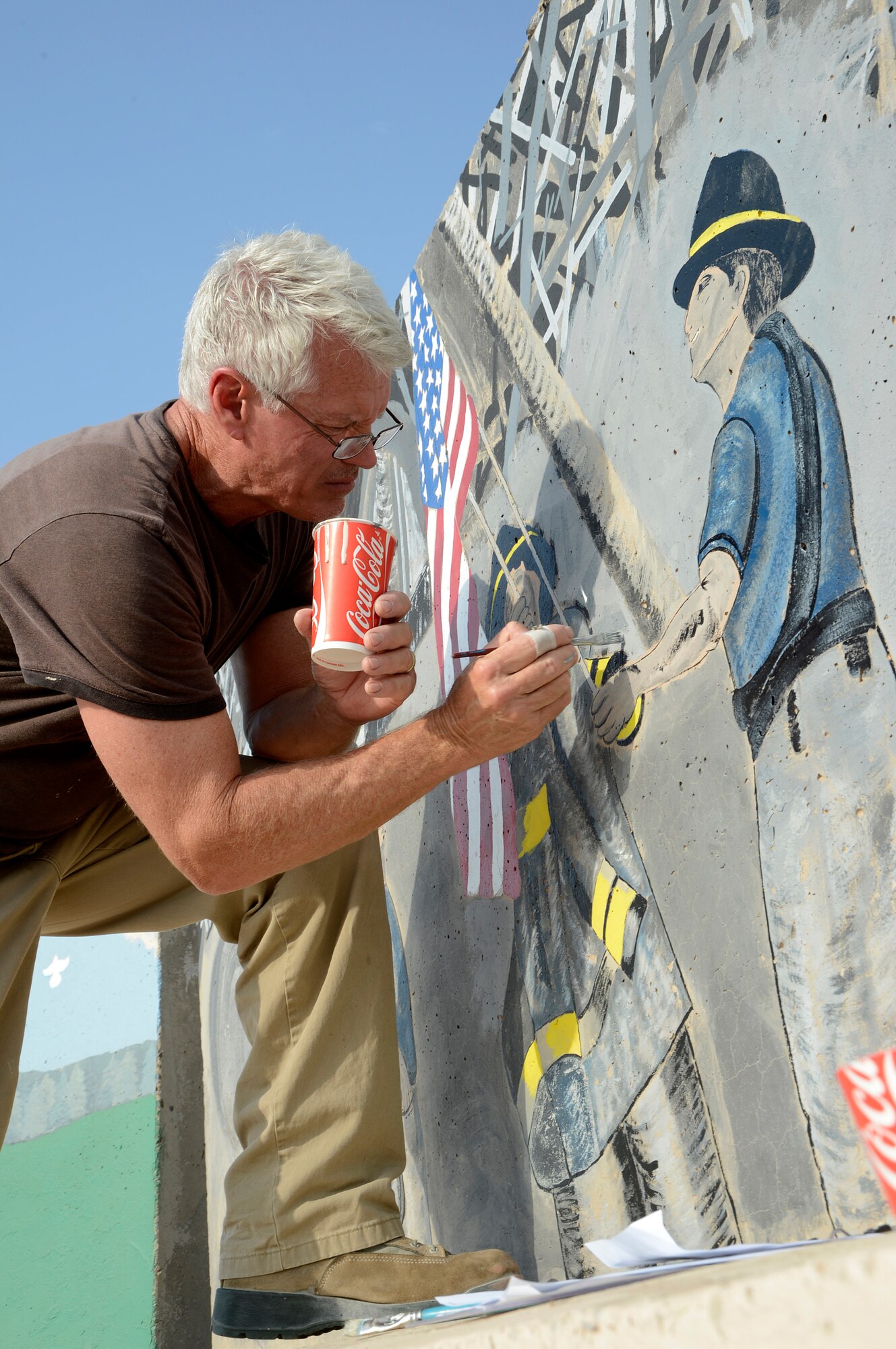 Mr. Mike May, 386th Expeditionary Communications Squadron, telephone installation and repair contractor, restores a memorial mural here, Sep 5, 2013. The memorial is the September 11 tri-wall that was initially painted in 2008. May is restoring this due to the degradation that has happened due to the years of wear and tear. He also has researched the images used to create the walls and is making minor changes to make the walls a little more authentic. May, a native of Tampa Fla. was asked by the first sergeants to work with them to bring the memorial back to life. (U.S. Air Force photo by Master Sgt. Christopher A. Campbell)