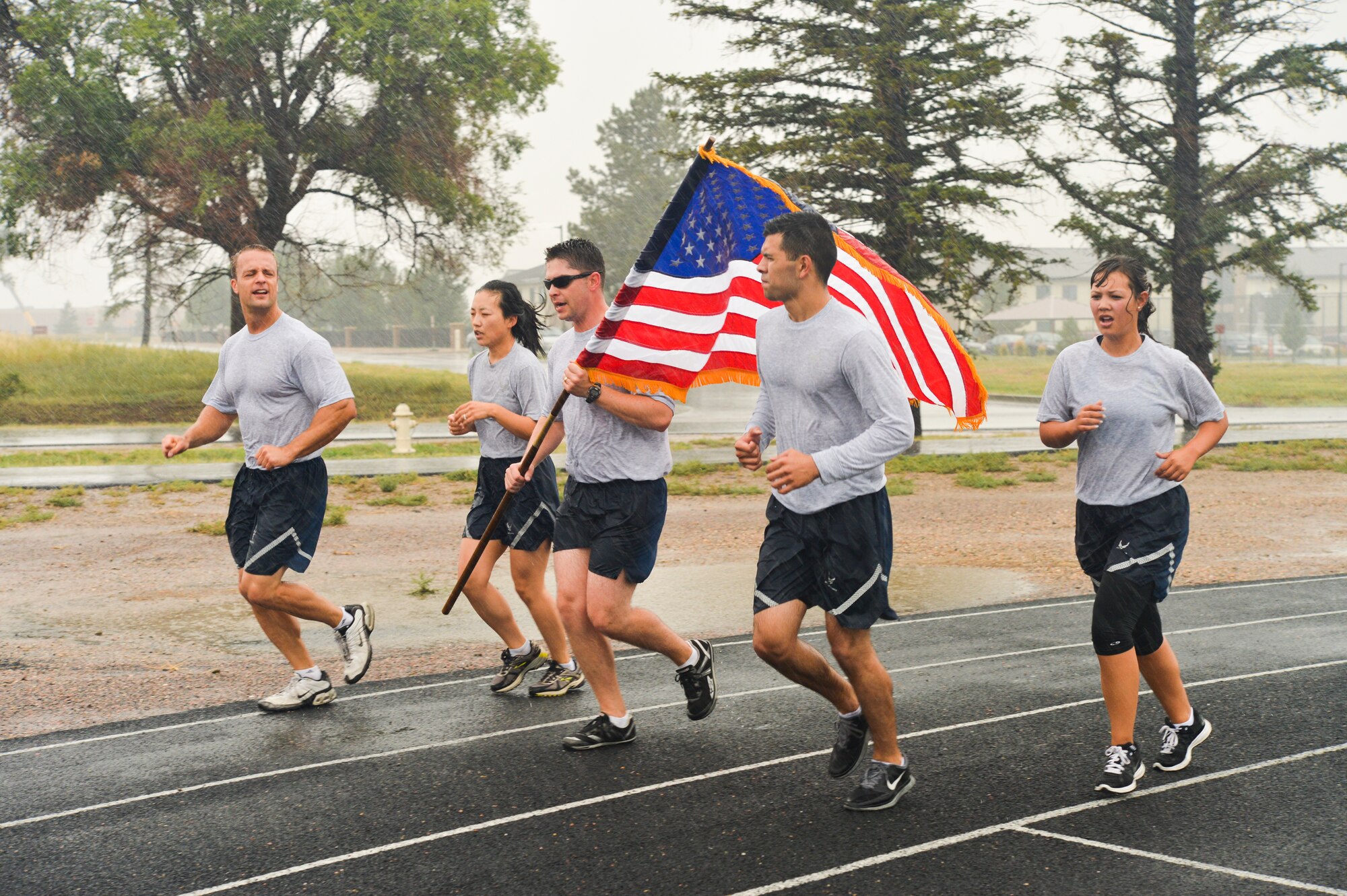 Capt. Eric McCutchen, 460th Space Wing legal office chief of military justice, carries the American Flag in the rain accompanied by wingman during the Patriot Day and National Day of Remembrance memorial run Sept. 11, 2013, on Buckley Air Force Base, Colo. Team Buckley members participated in a 10 hour run to remember those who died in the 9/11 attacks. (U.S. Air Force photo by Staff Sgt. Paul Labbe/Released)