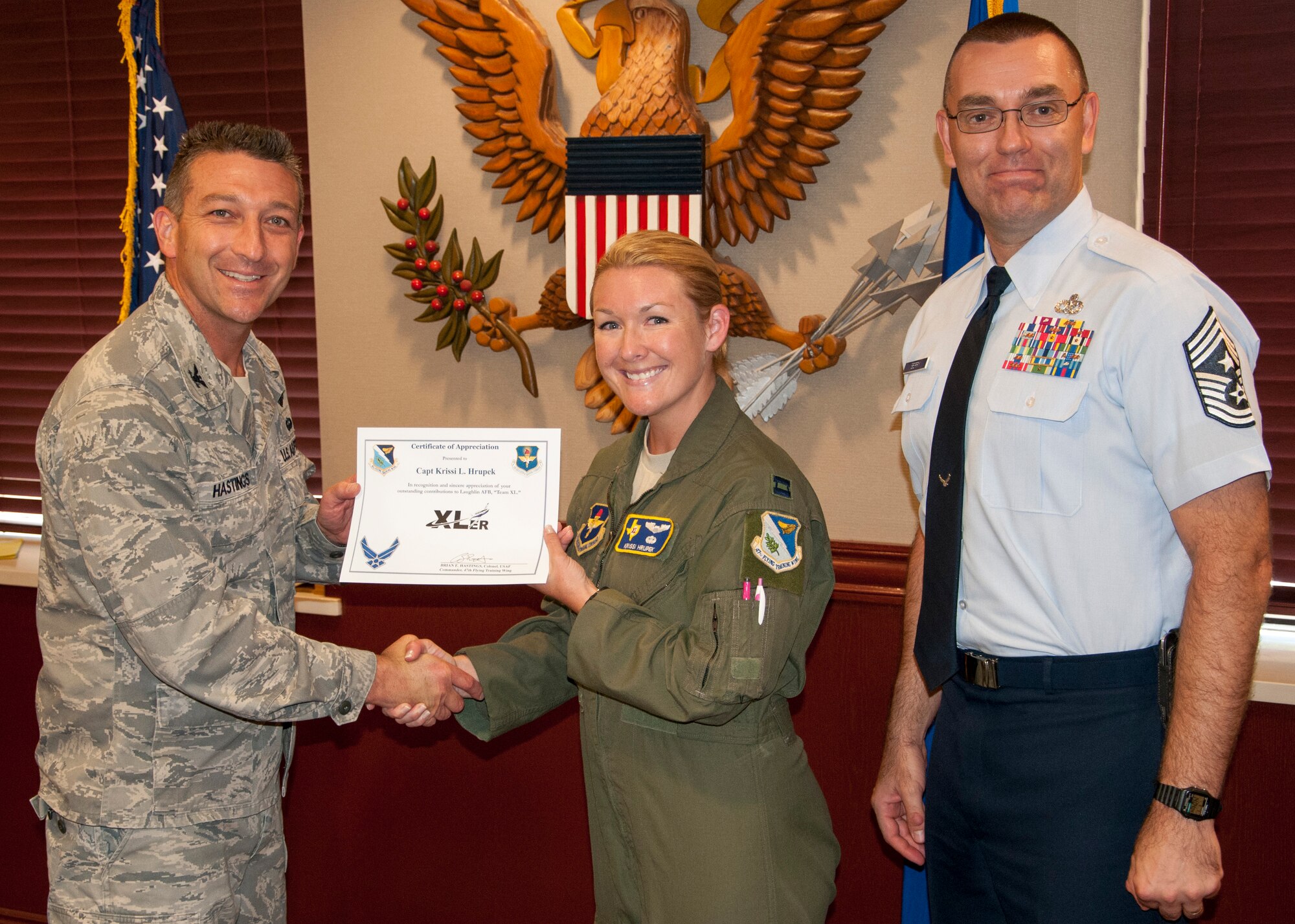 Capt. Krissi Hrupek, 47th Flying Training Wing T-6A Texan II Flight Safety officer, poses with Col. Brian Hastings, 47th Flying Training Wing commander, and Chief Master Sgt. Garry Berry, 47th FTW command chief, after being presented the XLer of the week award here Sept. 3, 2013. The XLer is a weekly award chosen by wing leadership and given to those who consistently make outstanding contributions to Laughlin and their unit. (U.S. Air Force photo/Joel Langton)