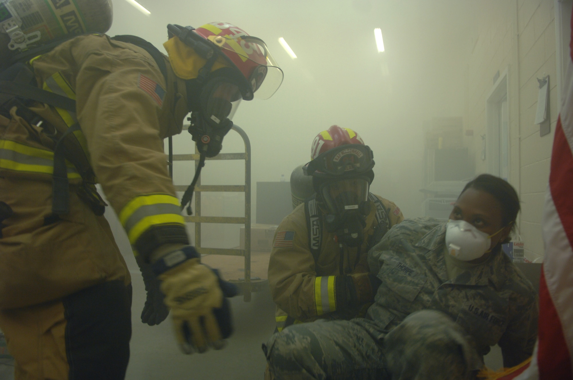 U.S. Air Force Staff Sgt. Candice Thorpe, right, 100th Communications Squadron NCO in charge of parcel customer service from Dover, Del., is “rescued” by Team Mildenhall firefighters Sept 9, 2013, at the post office on RAF Mildenhall, England. As part of an operational readiness inspection, a mock fire exercise was conducted in the post office. Simulated victims were placed around the post office under cover of thick fake smoke in order to make the scenario as realistic as possible. (U.S. Air Force photo by Airman 1st Class Dillon Johnston/Released)