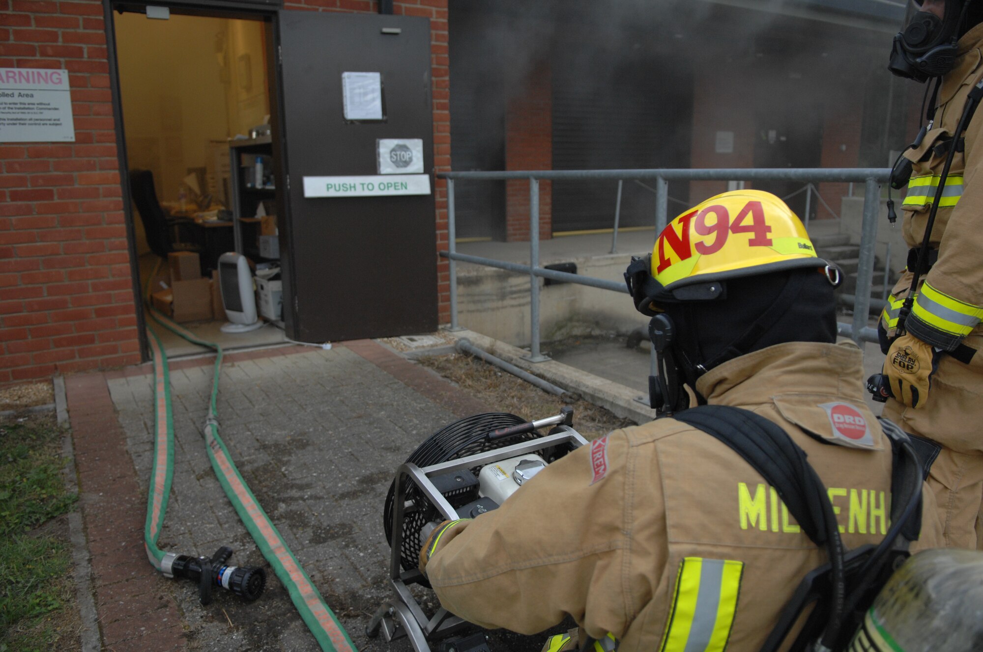 Andrew Nash, 100th Civil Engineer Squadron Fire Department firefighter, directs airflow from a fan into the post office Sept. 9, 2013, on RAF Mildenhall, England. Following a mock fire exercise at the post office, firefighters worked to clear the fake smoke from the building. Firefighters responded to the incident, retrieved simulated casualties and extinguished the fire. (U.S. Air Force photo by Airman 1st Class Dillon Johnston/Released)