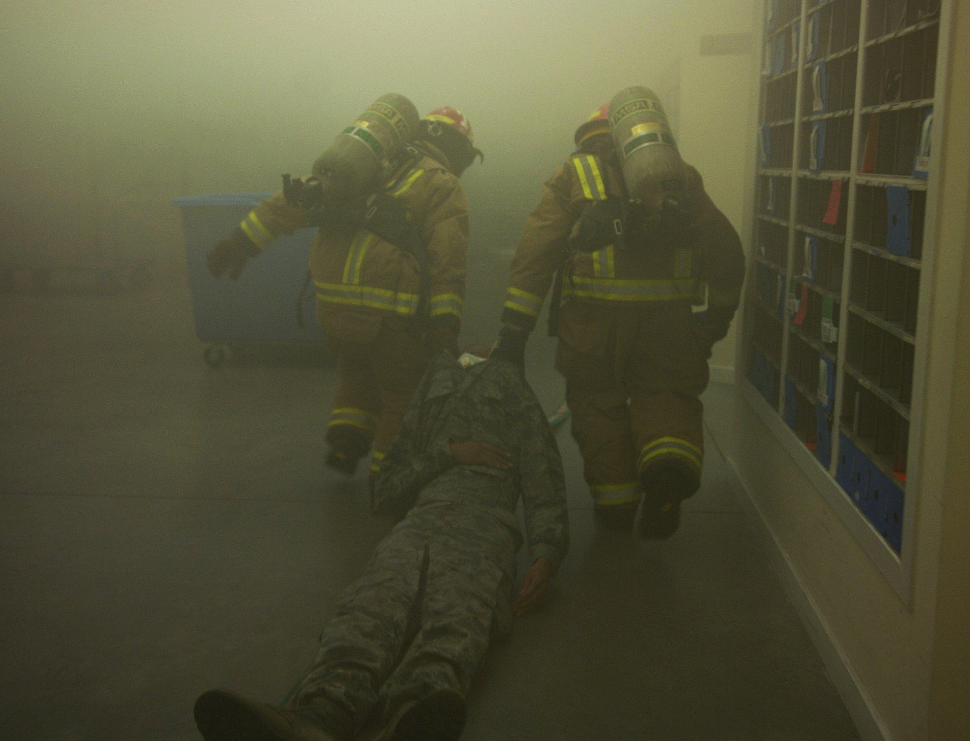 U.S. Air Force Tech. Sgt. Melvin Adkins, 100th Communications Squadron postmaster from Moreno Valley, Calif., is dragged from the post office by Team Mildenhall firefighters Sept. 9, 2013, on RAF Mildenhall, England. Firefighters responded to a simulated fire in the post office as part of an operational readiness inspection for RAF Mildenhall. The exercise was aimed at testing the response time and search and rescue capabilities of the firefighters. (U.S. Air Force photo by Airman 1st Class Dillon Johnston/Released)