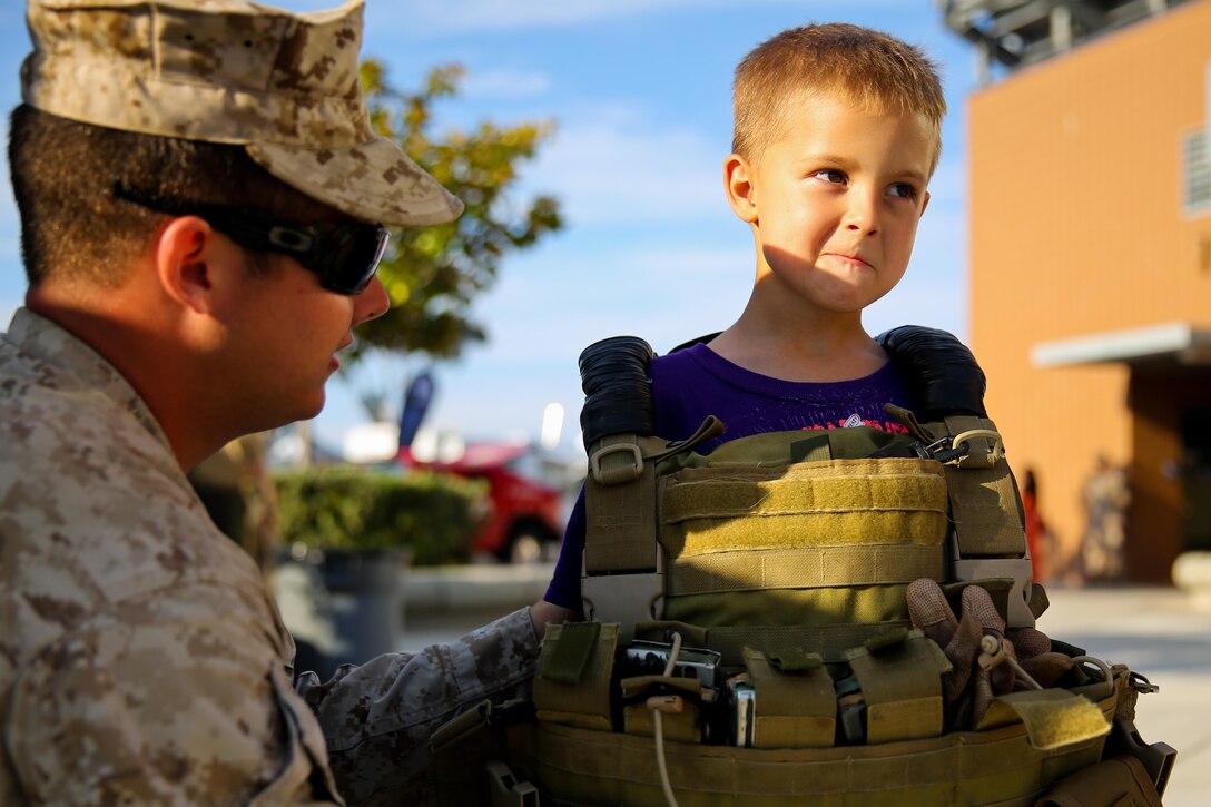 Damian Reed, 5, tries on a flak jacket with the help of Navy Petty Officer 3rd Class Shane Brown, a corpsman with Kilo Company, 3rd Battalion, 5th Marine Regiment, during the Honor Bowl here, Sept. 6, 2013. Brown, a native of Lacey, Wash., showcased his medical equipment as part of a static display put together by the battalion. The Saturday night game honored the Marines and their families who served with the battalion.