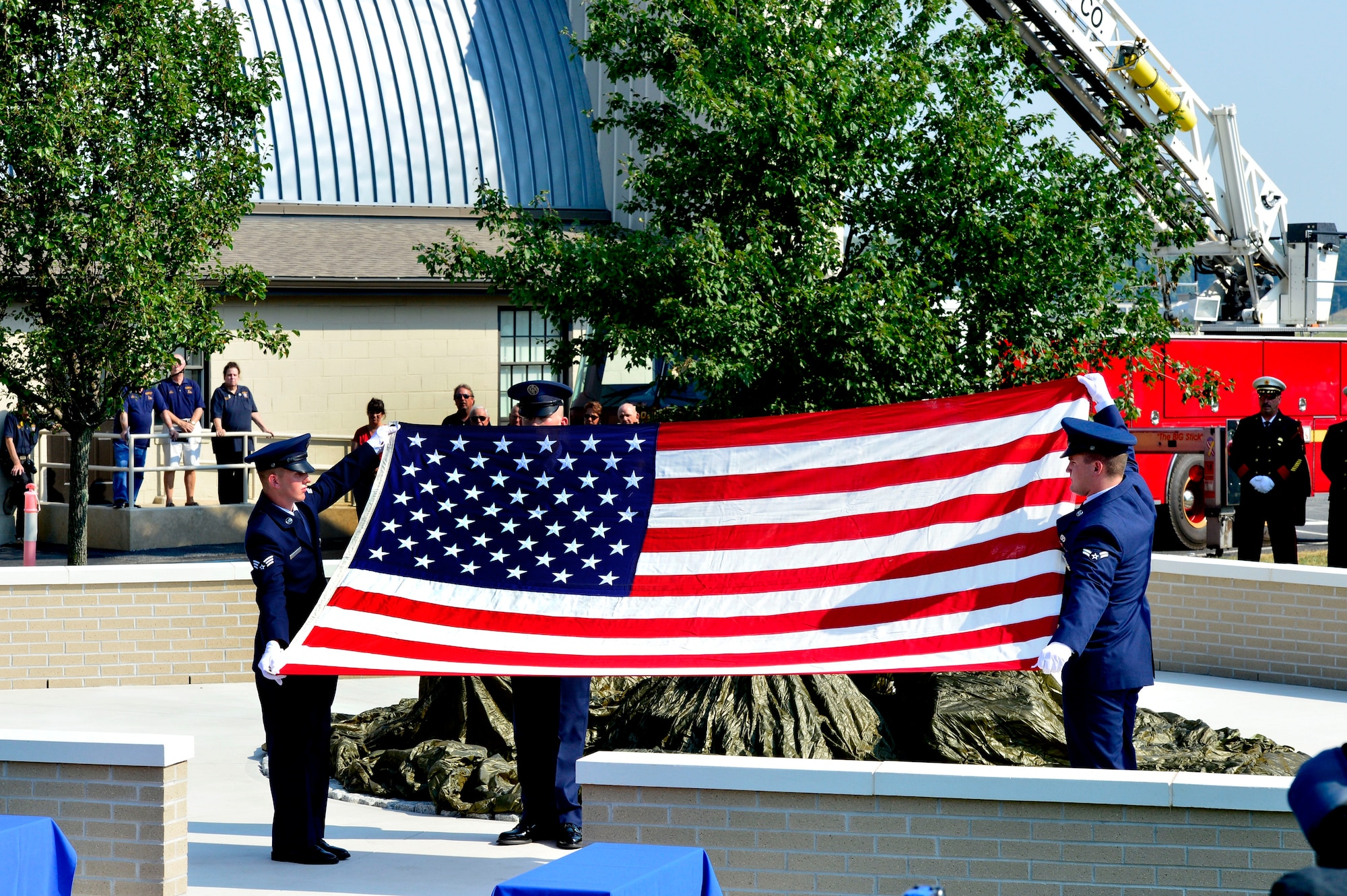 Senior Airman Joshua Bosley, left, Airman Marc Green, center, and Airman 1st Class Dallas Gullion all of the 436th Civil Engineer Squadron fire department, fold the flag at the dedication of the Sept. 11 Memorial Sept. 11, 2013, at the Air Mobility Command Museum on Dover Air Force Base, Del. The memorial, which incorporates two pieces of steel from World Trade Center tower one, a rock from the United Airlines Flight 93 crash site and a block from the damaged portion of the Pentagon, was unveiled at the ceremony. (U.S. Air Force photo/David S. Tucker)