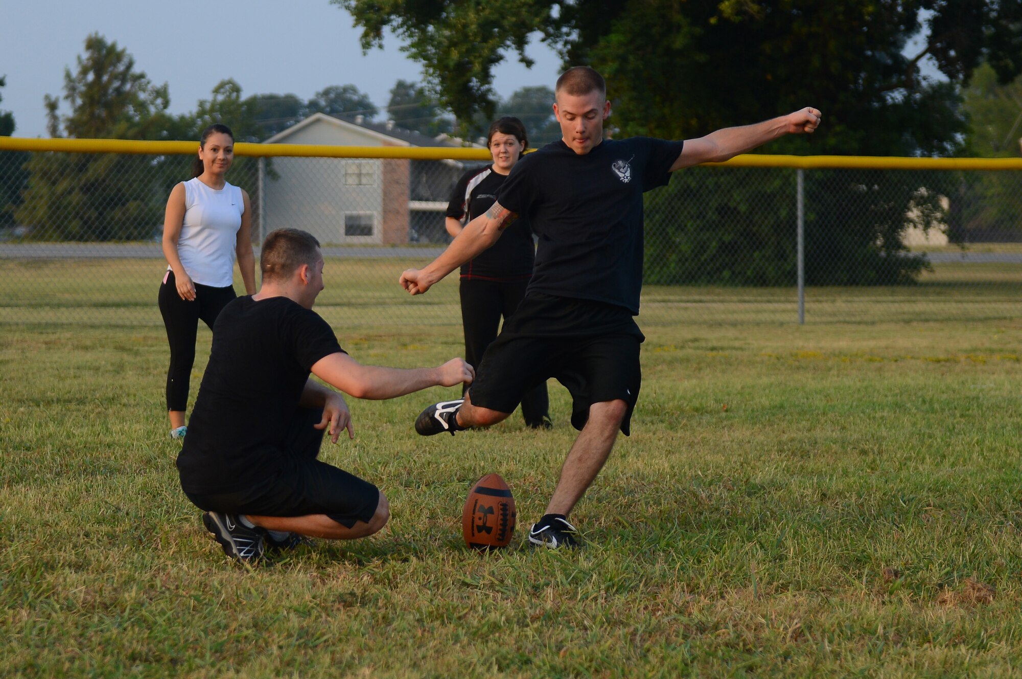 Senior Airman Kent Pendleton holds a football as Senior Airman Daniel Speed, 2nd Contracting Squadron contracting specialists, kicks off on Barksdale Air Force Base, La., Sept. 13, 2013. Along with playing ultimate football, Airmen from the 2nd CONS had briefings and watched videos about team work and stress as a part of Wingman Week. (U.S. Air Force photo/Senior Airman Micaiah Anthony)
