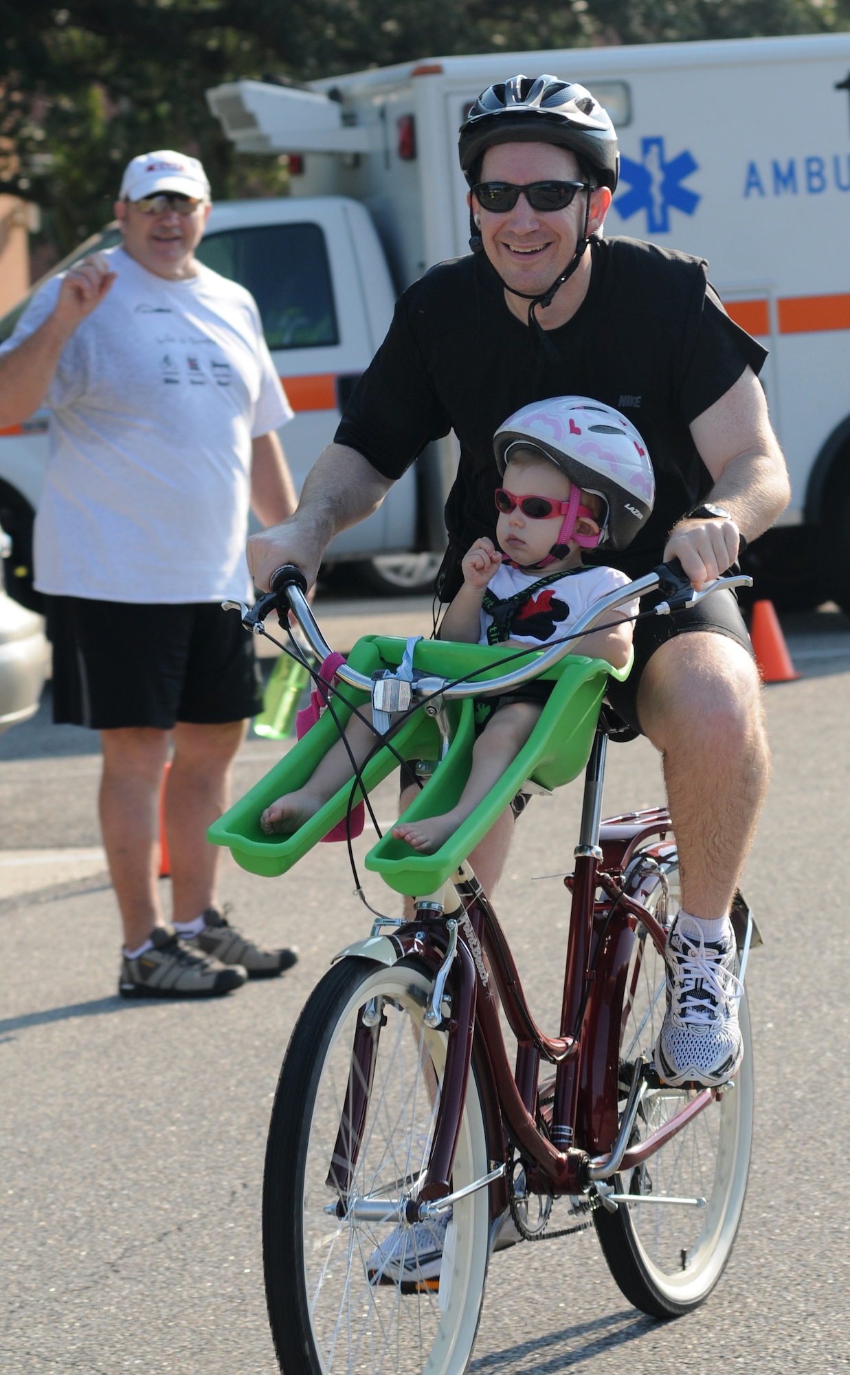 Roger Milford, 81st Force Support Squadron, cheers on Craig Dunham, 81st Training Wing, and his daughter as he cycles around the 9-mile bike course during Keesler's mini-triathlon Sept. 13, 2013, at Keesler Air Force Base, Miss.  The event also included a 2-mile run and a 200-yard swim.  (U.S. Air Force photo by Kemberly Groue)