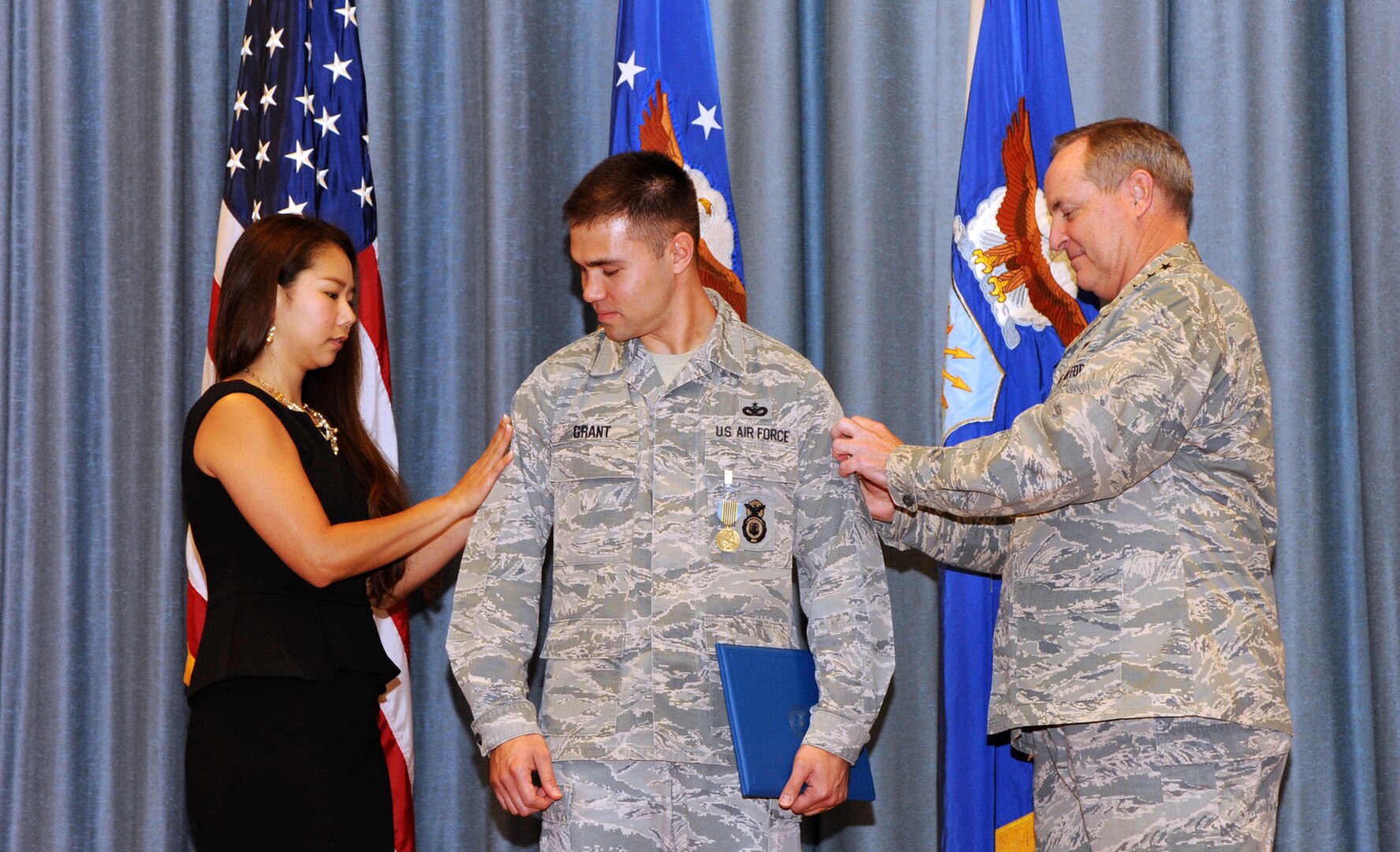Eriko Grant, wife of Edward Grant, at left; and Air Force Chief of Staff Gen. Mark A. Welsh III, far right; tack technical sergeant stripes onto the sleeves of Edward Grant during an All Call at Joint Base San Antonio-Randolph’s Fleenor Auditorium Sept. 12.  Before the promotion, Welsh presented Grant with the Airman’s Medal, given to service members or those of a friendly nation while serving in any capacity with the U.S. Air Force distinguishing themselves with heroic actions, usually at the voluntary risk of their lives. Grant is a defender with the 902nd Security Forces Squadron at JBSA-Randolph. (U. S. Air Force photo by Melissa Peterson)
