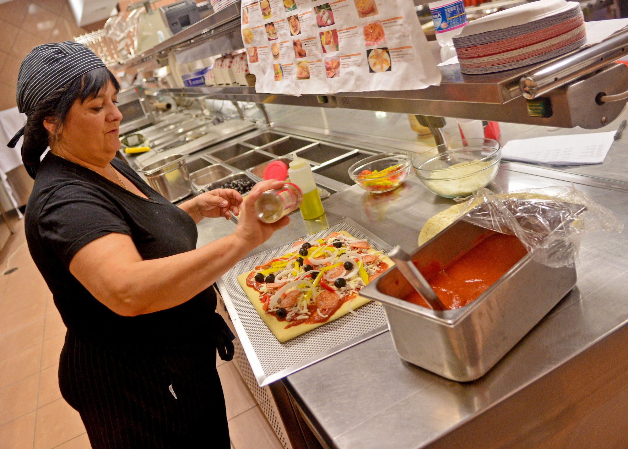 Mary Ann Lauro, 31st Force Support Squadron chef and kitchen manager, sprinkles oregano on a pizza, Sept. 4, 2013, at Aviano Air Base, Italy. The pizza will be added to the La Bella Vista club’s bar menu Sept. 13, and customers will be able to place pick-up orders over the phone and for lunch starting Sept. 24. (U.S. Air Force photo/Senior Airman Briana Jones)