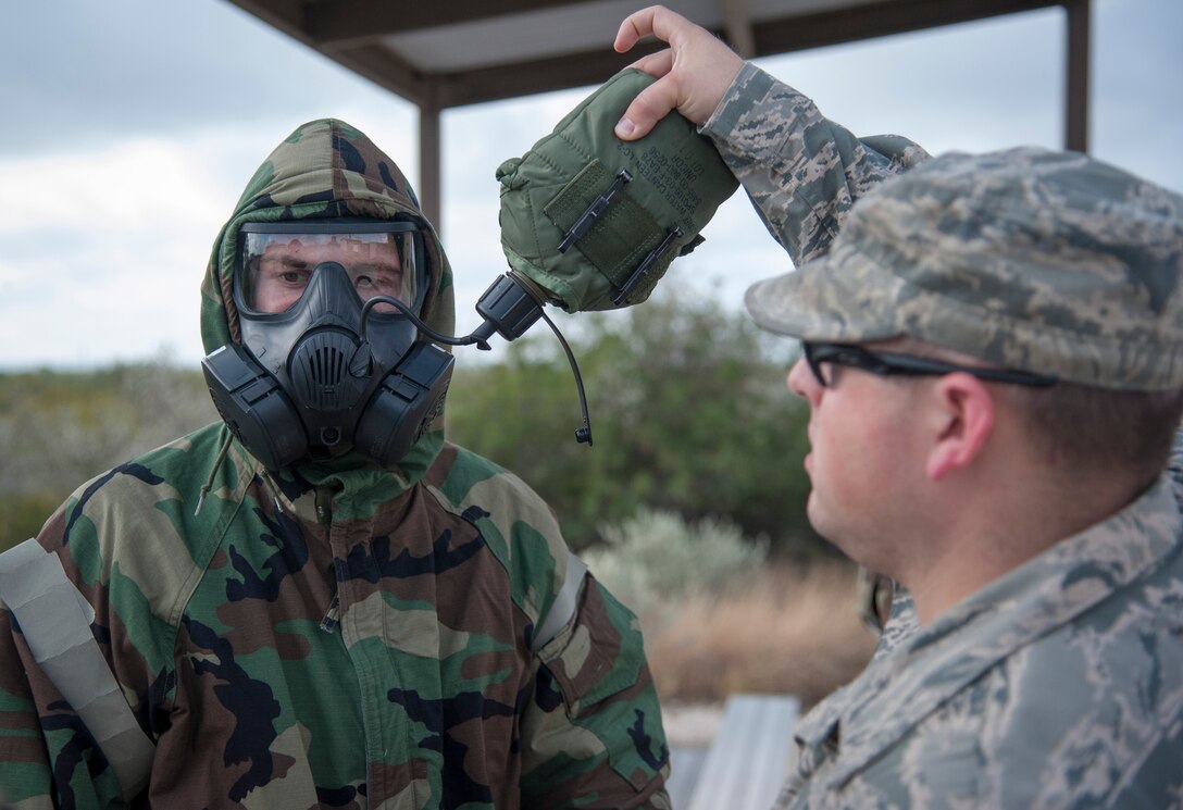 Staff Sgt. Theodore Van De Sample, 47th Civil Engineer Squadron readiness and emergency flight NCO in charge, right, helps 2nd Lt. Charles Heim, 47th Civil Engineer Squadron officer in charge of emergency management, drink from his canteen during a chemical, biological, radiological and nuclear training course at Laughlin Air Force Base, Texas, Sept. 12, 2013. Each person attending the course needed to show proficiency in drinking from a canteen while wearing a gas mask. (U.S. Air Force photo/Senior Airman John D. Partlow)