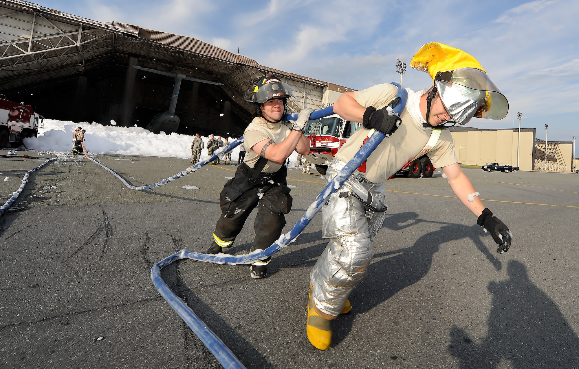 Airman Justin Cromwell and Airman 1st Class Alexander McDonald, from the 436th Civil Engineer Squadron, Fire Department, pull a hand hose from the foam spilling out of hangar 706 on Sept. 16, 2013 at Dover Air Force Base, Del. The Dover Fire Department responded to the inadvertent release of fire suppression foam in hangar 706 and the firefighters used water to dissipate the foam. (U.S. Air Force photo/Greg L. Davis)