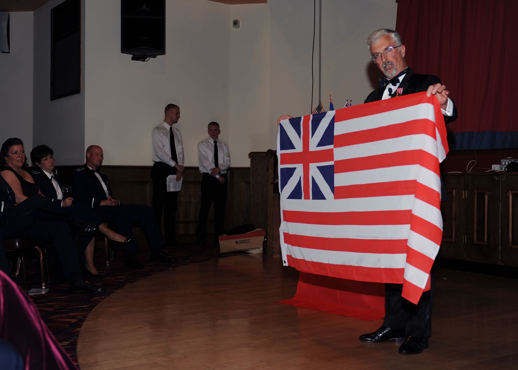 Bruce Wynn, Retired Royal Air Force Air Cdre. (Brig. Gen. equivalent) and honorary commander speaks to Team Mildenhall members celebrating the U.S. Air Force's birthday Sept. 14, 2013, during the Air Force Ball on RAF Mildenhall, England. Wynn is holding the Grand Union Flag from 1776 in his hands. The official birthday is Sept.  18, marking the 66th annual celebration of the U.S. Air Force becoming its own separate branch of the U.S. military. (U.S. Air Force photo by Airman 1st Class Preston Webb/Released)
