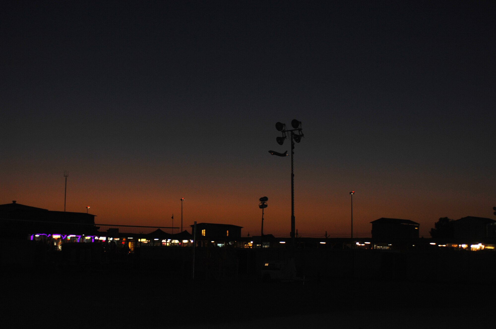 The Kandahar Boardwalk is lit up during the night of Sept. 7, 2013, at Kandahar Airfield, Afghanistan, as an aircraft takes off in the back drop. The planned, gradual closure of vendors at the boardwalk is the only piece of this iconic morale venue closing, as the recreation fields and plywood boardwalk will remain after the vendors have departed. (U.S. Air Force photo/Senior Airman Jack Sanders)