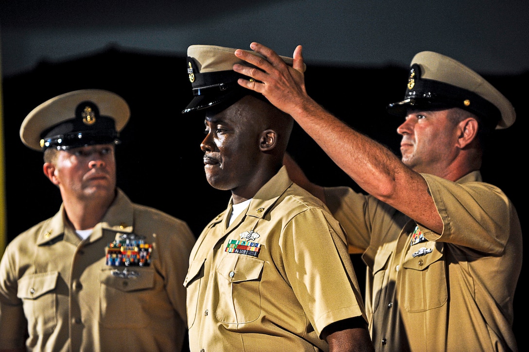 U.S. Navy Senior Chief Petty Officer James Strong, right, places a cover on U.S. Navy Chief Roderick Nelson, center, during a pinning ceremony for chief petty officers on Camp Lemonnier in Djibouti, Sept. 13, 2013. Nelson is an equipment operator.