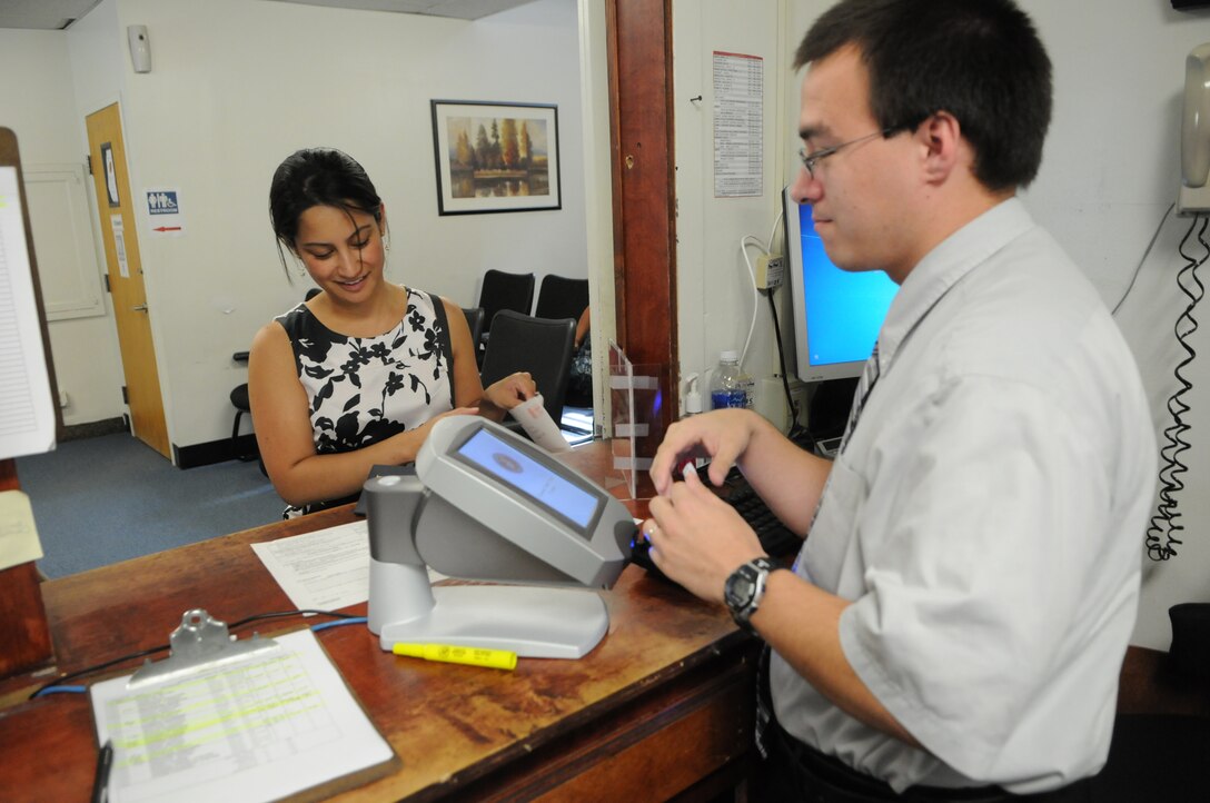 Scott Sutton, verifying official at the Defense Enrollment Eligibility Reporting System ID Card Center, uses the center’s new queue-management system to print a ticket for Marine Corps spouse Jessica Bukovac. The system is the same used in the Department of Motor Vehicles. 