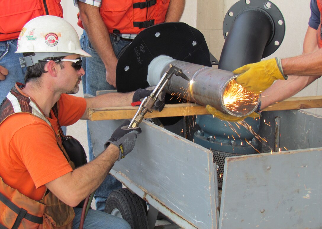 A welder uses a cutting torch to trim an intake pipe for the hydro plant.