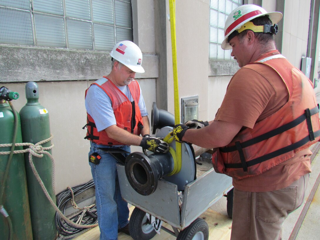 Two workers secure the rigging on an intake pipe that will be lowered into the water and installed by divers.