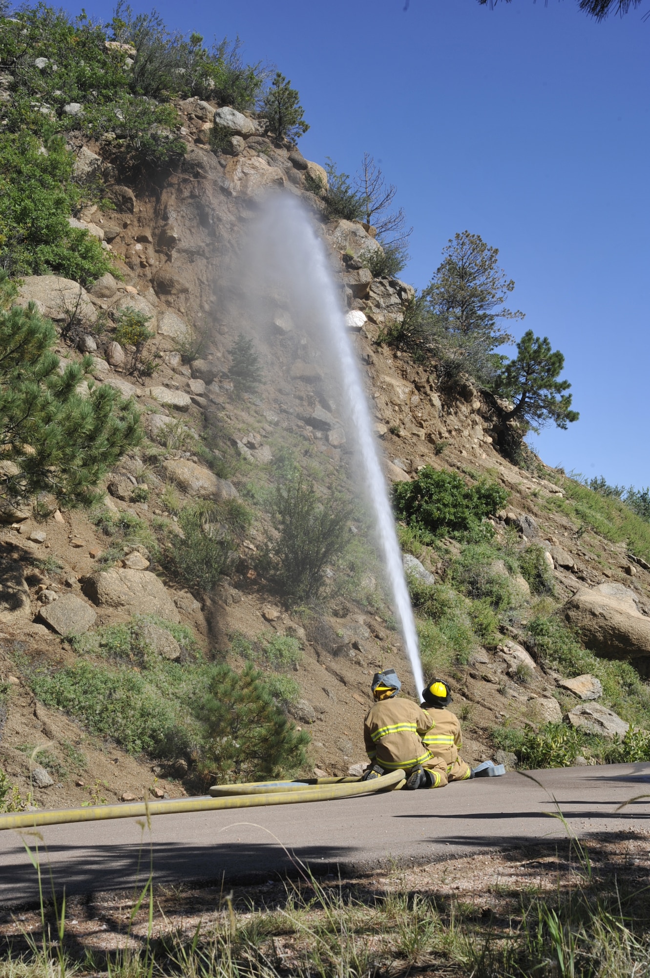 CHEYENNE MOUNTAIN AIR FORCE STATION, Colo. – Fire fighters from the 721st Mission Support Group spray water onto an unstable mountainside Sept. 17, to clear rock after a mudslide deposited nearly 5,000 cubic yards of debris in front of the main entrance of CMAFS. Despite the rockslide, the air defense, space surveillance and missile warning missions inside of the mountain remained 100 percent operational. (U.S. Air Force photo/Rob Lingley)