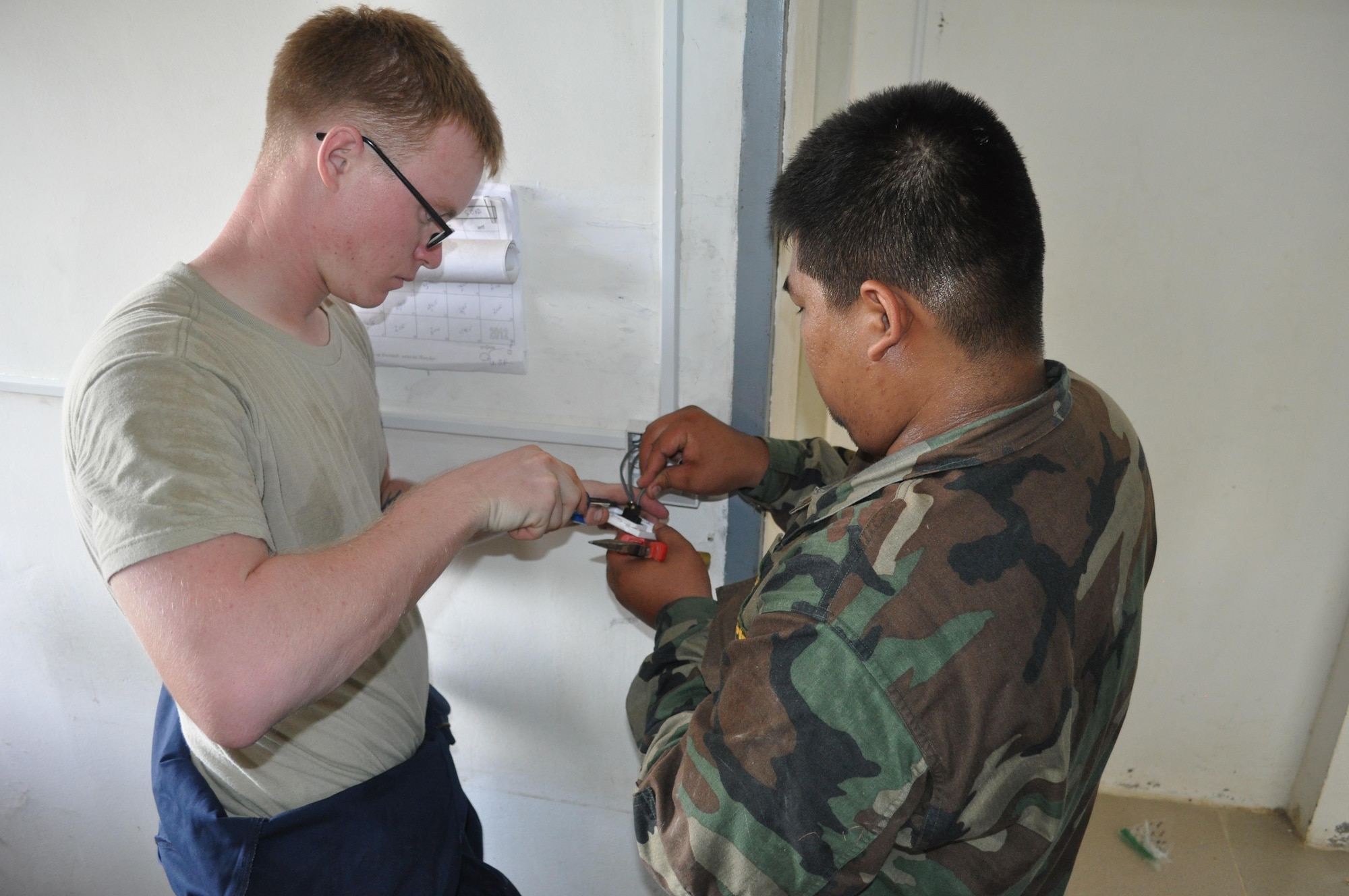 Senior Airman Timothy Janca, electrician from the 18th Civil Engineer Squadron, Kadena Air Base, Japan, installs a light switch with electrician Sgt 2nd Class Sat Sovannarith, Royal Cambodian Armed Forces at a health center Sept. 11, 2013, during Operation Pacific Angel 13-5 at Takeo Province, Cambodia. The health center is one of three undergoing renovations. Thirty-six U.S. forces and RCAF have teamed up to complete renovations scheduled to end September 14. 