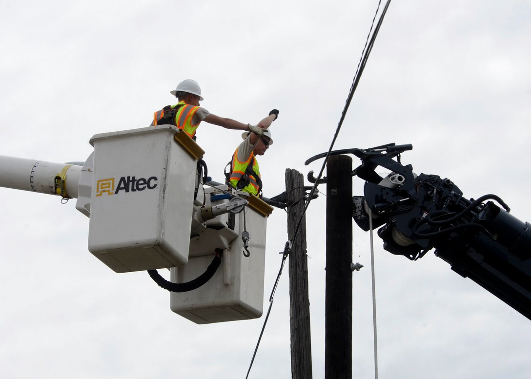 Airman 1st Class Kaleb Johnson (left) and Senior Airman Josh Kohler, 28th Civil Engineer Squadron electrical systems technicians, uses hard signals to direct the operator of a high reach truck during the installation of a new utility pole as part of an equipment upgrade at Ellsworth Air Force Base, S.D., Sept. 13, 2013. Electrical systems technicians use high reach trucks to work on power lines and street lights throughout the base. (U.S. Air Force photo by Airman 1st Class Anania Tekurio/Released)