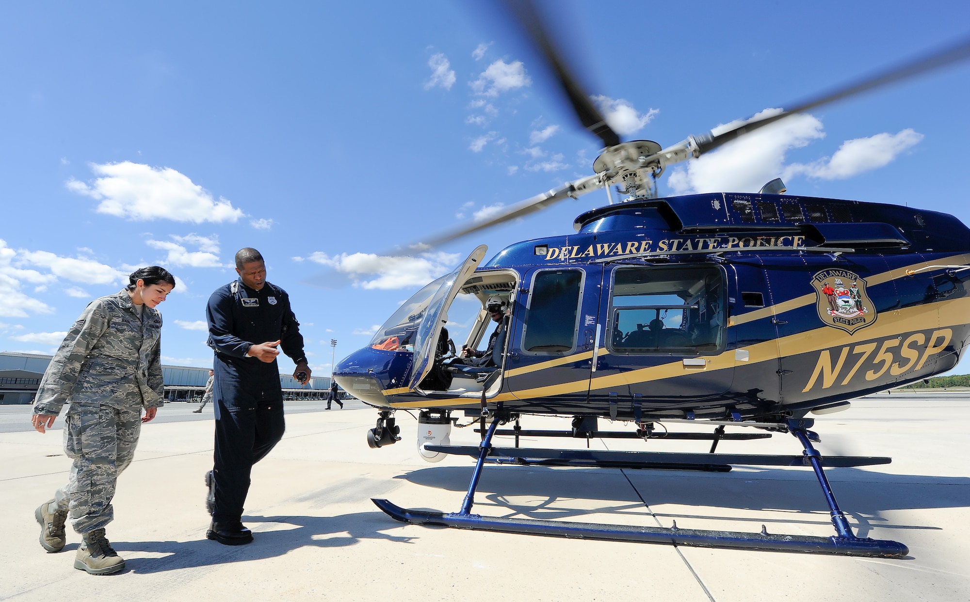 Staff Sgt. Vanessa Baer of the 436th Operations Support Squadron, radar approach control section, is escorted out to a Delaware State Police Bell 407 helicopter by Trooper (pilot) Mike Branch for a familiarization flight from Dover Air Force Base, Del. on Sept. 18, 2013. RAPCON controllers and other air traffic control personnel gained insight in to the world of helicopter operations through a briefing and orientation flight with the Delaware State Police, aviation section. (U.S. Air Force photo/Greg L. Davis)
