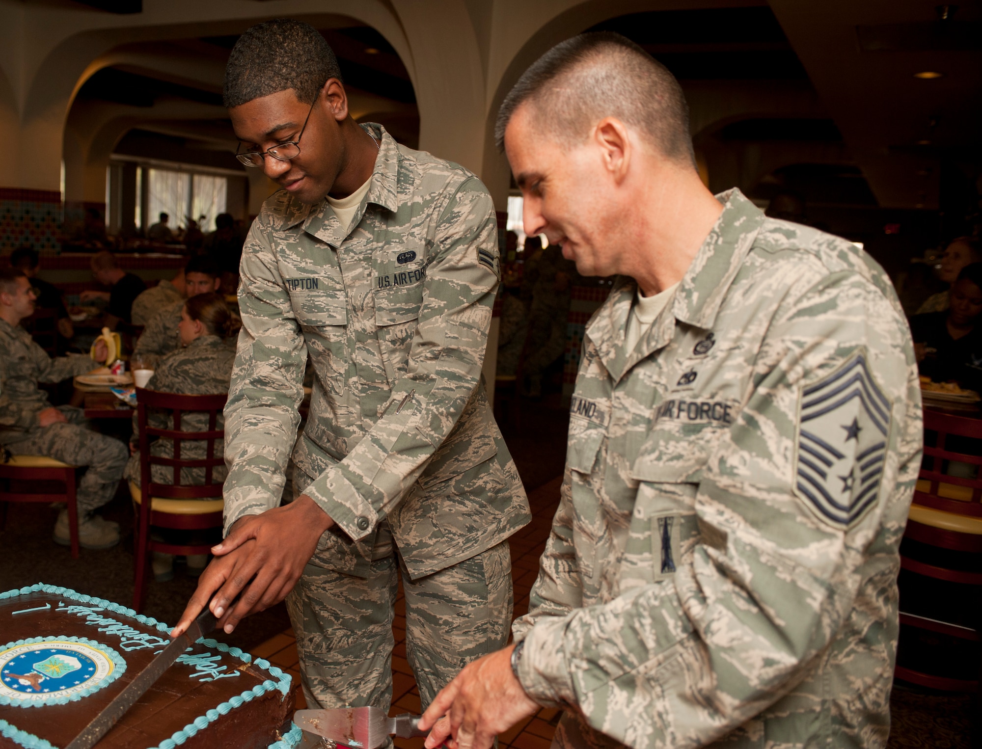 Chief Master Sgt. Steven Cleveland, 99th Air Base Wing command chief, and Airman 1st Class Timothy Tipton, 99th Communication Squadron wing information assurance officer, cut an Air Force 66th birthday cake at the Crosswinds Dining Facility Sept. 18, 2013, at Nellis Air Force Base, Nev. The two youngest Airmen in the dining facility were asked to join two most senior ranking members of the 99th ABW to cut the cake. (U.S. Air Force photo by Staff Sgt. Michael Charles)