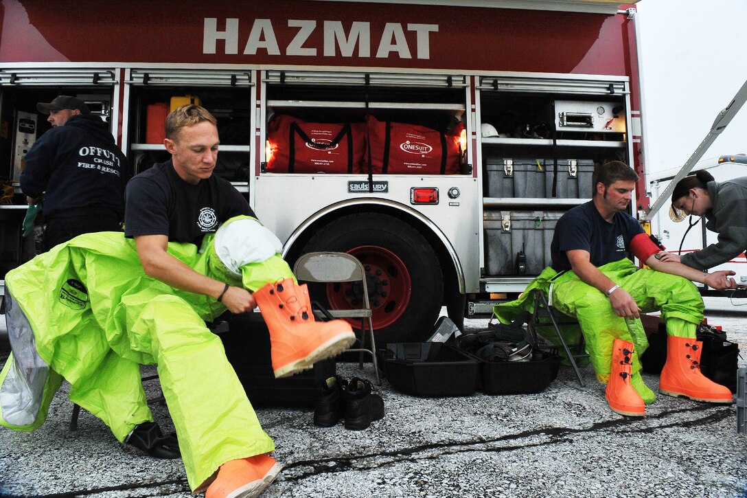 Jason Livermore puts on his chemical suit while Ronald Dawson, both firefighters with the 55th Civil Engineer Squadron, gets his blood pressure checked by U.S. Air Force Staff Sgt. Samantha Wendel, 55th Medical Operations Squadron medical technician, during a HAZMAT task evaluation as part of a Consolidated Unit Inspection Sept. 17 at Offutt Air Force Base, Neb. The 55th Wing took part in 11 inspections throughout the month of September. (U.S. Air Force photo by Charles Haymond/Released)