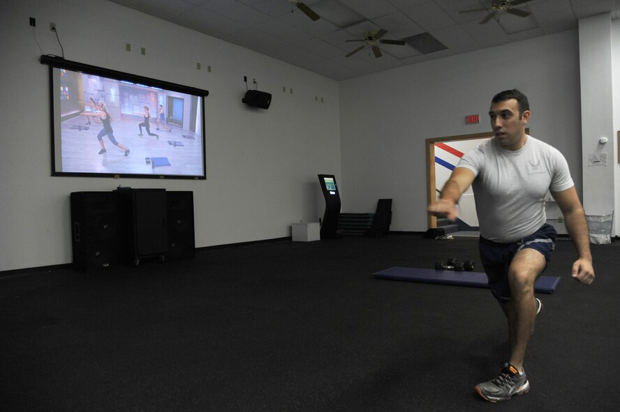 Senior Airman Jeremy Flores, 341st Force Support Squadron services journeyman, lunges during a Kinetics 350 workout at the Malmstrom Fitness Center on Sept. 17. The Air Force recently installed “Fitness on Request” kiosks at 66 installations, to supplement in-person aerobics classes. The kiosk contains more than 50 exercise videos running between 20 to 60 minutes, and is updated every quarter. (U.S. Air Force photo/Senior Airman Katrina Heikkinen) 