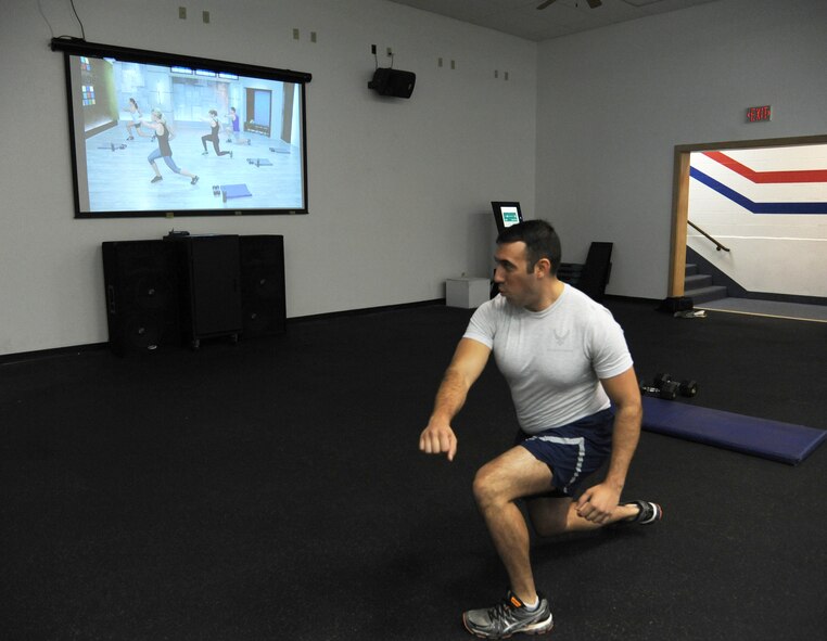 Senior Airman Jeremy Flores, 341st Force Support Squadron services journeyman, lunges during a Kinetics 350 workout at the Malmstrom Fitness Center on Sept. 17. The Air Force recently installed “Fitness on Request” kiosks at 66 installations, to supplement in-person aerobics classes. The kiosk contains more than 50 exercise videos running between 20 to 60 minutes, and is updated every quarter. (U.S. Air Force photo/Senior Airman Katrina Heikkinen) 