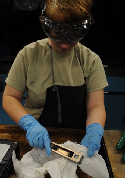 Senior Airman Sherry Phillips, 2nd Maintenance Squadron non-destructive inspection journeyman, wipes off oil bath particles from a piece of equipment on Barksdale Air Force Base, La., Sept. 19, 2013. The liquid is used to detect small cracks on the part that would be missed by the human eye. (U.S. Air Force photo/Senior Airman Benjamin Gonsier)