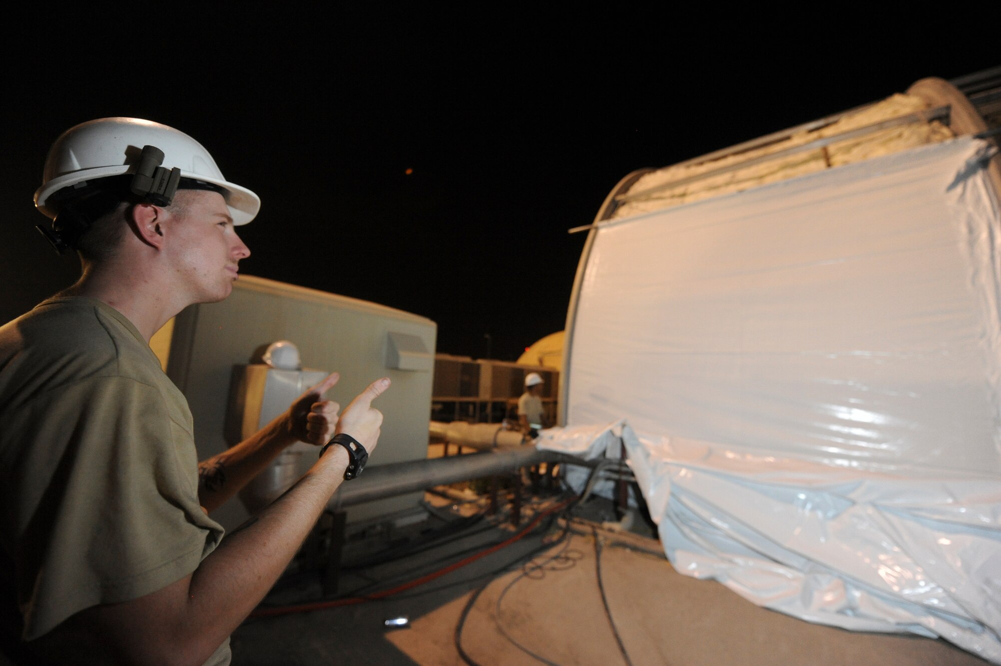 U.S. Air Force Senior Airman David Muncean-Deafenbaugh, uses hand signals to tell co-workers if the outer skin is being raised evenly. The skin was pulled into place by a vehicle inside the hangar, hand signals are the main way of communication between the engineers during this process. Muncean-Deafenbaugh is native to Ft. Drum, N.Y. and is deployed from Spanghelem Air Base, Germany. (U.S Air Force photo by Staff Sgt. Joshua J. Garcia)