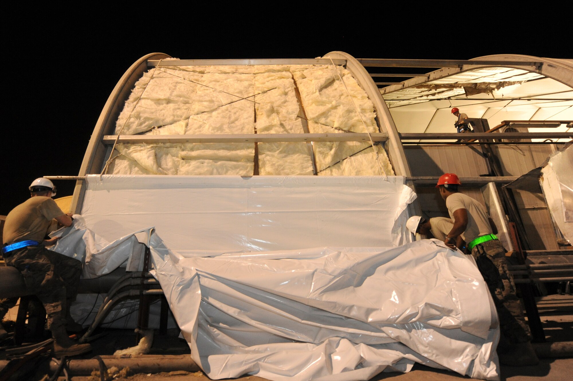 Airmen from the 577th Expeditionary PRIME BEEF Squadron, hand guide an outer skin to a hangar during renovations at an undisclosed location in Southwest Asia Sept. 2, 2013. The outer skin has to be hand-guided when the skin is first applied to ensure that it is evenly placed over the hangar. (U.S. Air Force photo by Staff Sgt. Joshua J. Garcia)