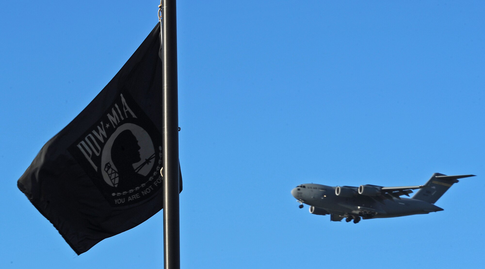 A Joint Base Pearl Harbor-Hickam C-17 Globemaster III flies past the prisoners of war/missing in action flag pole during the POW/MIA remembrance ceremony at Missing Man Formation, Joint Base Pearl Harbor-Hickam, Hawaii, Sept. 20, 2013. The C-17 Globemaster III is the newest, most flexible cargo aircraft to enter the airlift force.  (U.S. Air Force photo/Tech. Sgt. Jerome S. Tayborn)