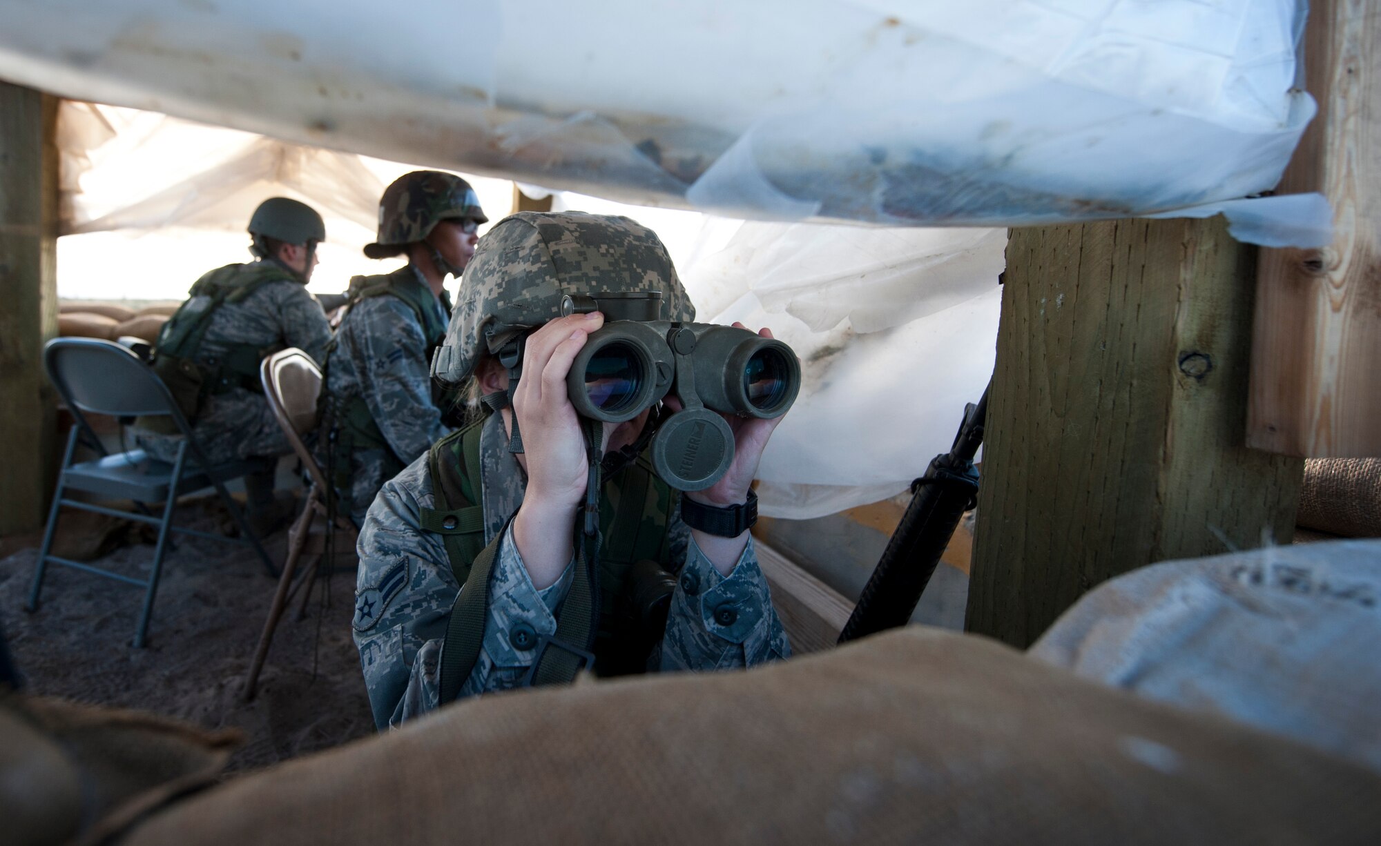 U.S. Air Force Airman 1st Class Courtney McFerrin, 726th Air Control Squadron command control battle management operations apprentice, looks through binoculars in a defensive fighting position Sept. 18, 2013, at Mountain Home Air Force Base, Idaho. Vigilance is a key component when providing base security. Airmen from the 726th ACS were given multiple scenarios to test their abilities in safe-guarding wingmen along with Air Force assets. (U.S. Air Force photo by Airman 1st Class Brittany A. Chase/Released)