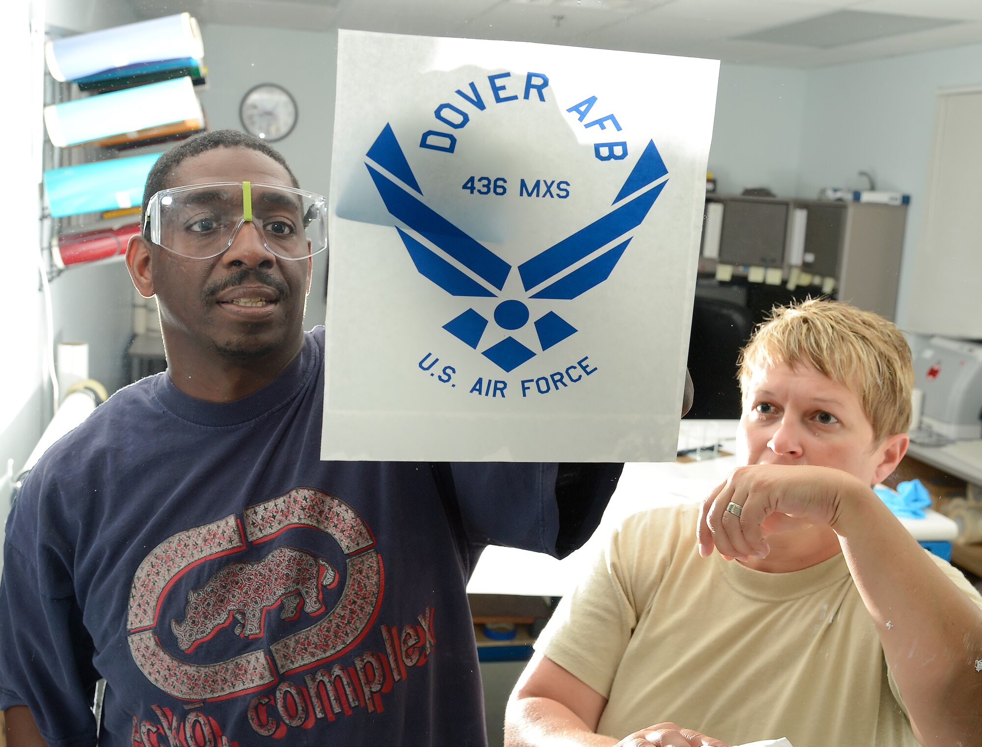 Antoine Robinson and Technical Sgt. Tracy Davis of the 436th Aircraft Maintenance Squadron corrosion control shop, apply a sign to an inside window on Sept. 9, 2013 at Dover Air Force Base, Del. Products made by the section include decals for windows, signs and aircraft. (U.S. Air Force photo/Greg L. Davis)