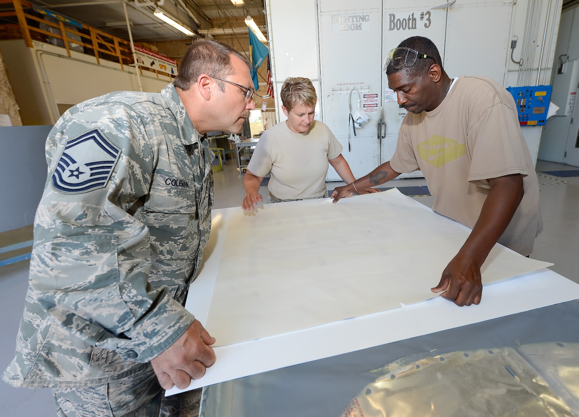 Senior Master Sgt. Earl Coleman (left) along with Technical Sgt. Tracy Davis and  Antoine Robinson carefully line-up a vinyl decal on a metal sheet during a sign project on Sept. 4, 2013 at Dover Air Force Base, Del. The project they are working on will be a mulit-colored Air Force Reserve Command badge once completed. (U.S. Air Force photo/Greg L. Davis)