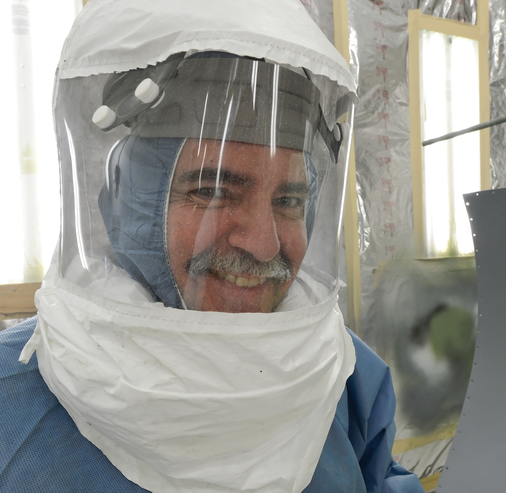 Peter Kalasky, Jr., a civilian employee of the 436th Maintenance Squadron, smiles broadly while working inside a climate-controlled paint booth while spraying primer on aircraft parts on August 28, 2013 at Dover Air Force Base, Del. Kalasky's protective equipment includes a positive pressure breathing hood.  (U.S. Air Force photo/Greg L. Davis)