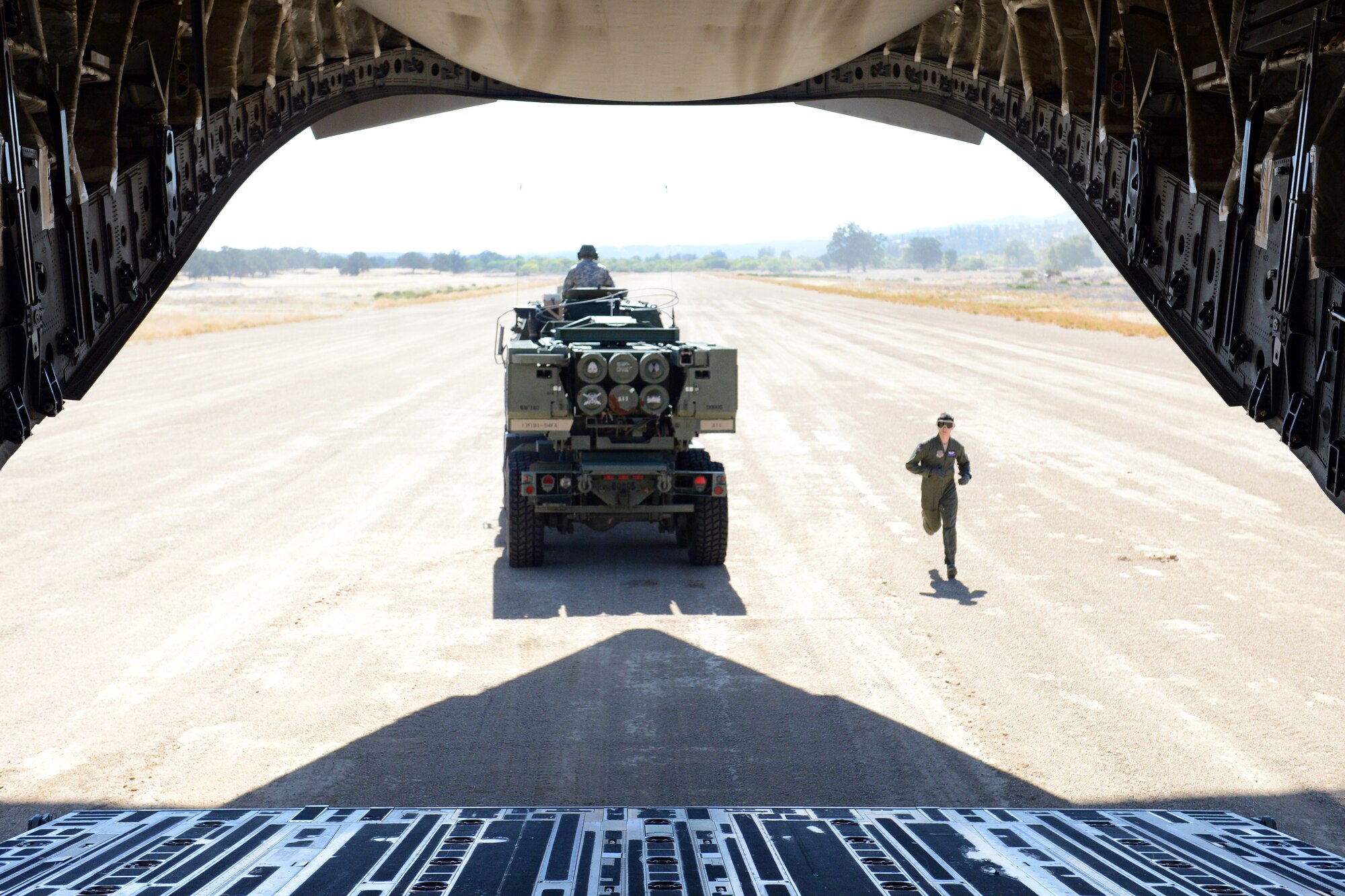 An M142 High Mobility Artillery Rocket System crew heads toward a designated firing point as Airman 1st Class Shaun Chapman, 4th Airlift Squadron loadmaster runs to unload the next crew Sept. 17, 2013, at Schoonover, Calif. Due to the 300 meter back-blast generated when a missile or rocket is launched from the unit, the HIMARS were required to be 500 yards away from the aircraft before the simulated live-fire was performed. (U.S. Air Force photo/Airman 1st Class Jacob Jimenez) 