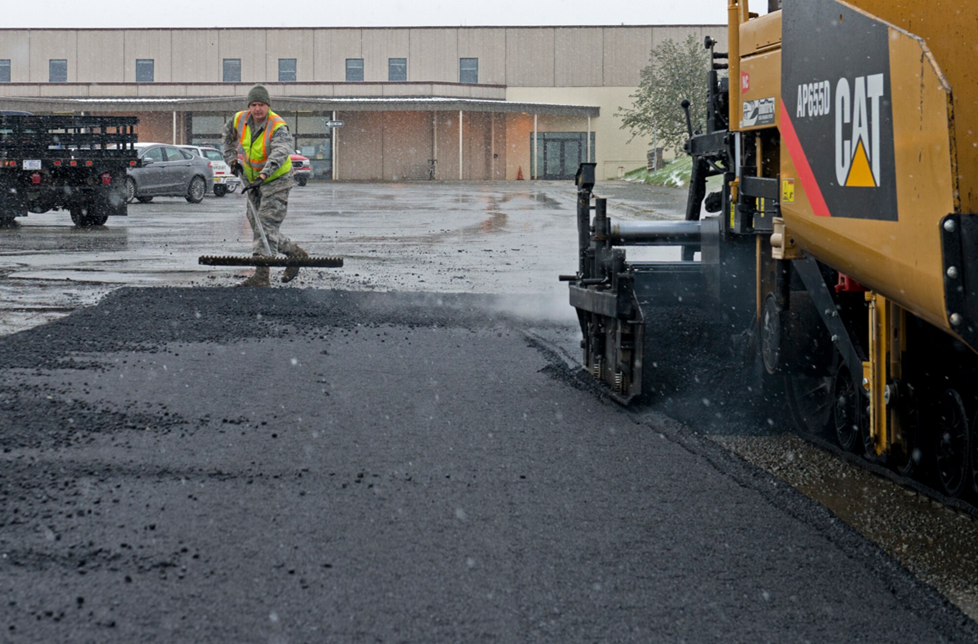 Senior Airman Eric Lippold, 773d Civil Engineer Squadron heavy equipment operator, evens the asphalt as they lay down pavement near the People's Center on Joint Base Elmendorf-Richardson, Sept. 23, 2013. Despite the early snowfall, the 773 CES was out working to repair roads. (U.S. Air Force photo/Staff Sgt. Zachary Wolf)