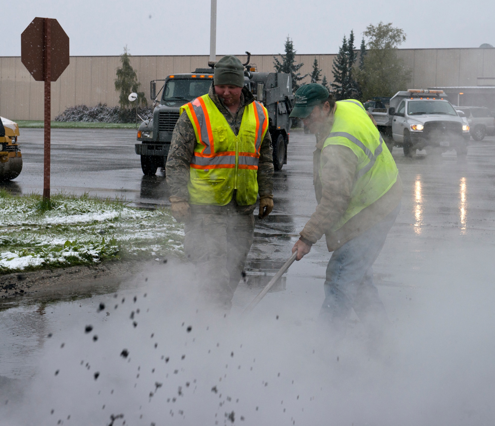 Senior Airman Eric Lippold (left) and Al Davis, both heavy equipment operators from the 773d Civil Engineer Squadron, even the asphalt as they lay down pavement near the People's Center on Joint Base Elmendorf-Richardson, Sept. 23, 2013. Despite the early snowfall the 773 CES was out working to repair roads. (U.S. Air Force photo/Staff Sgt. Zachary Wolf) 