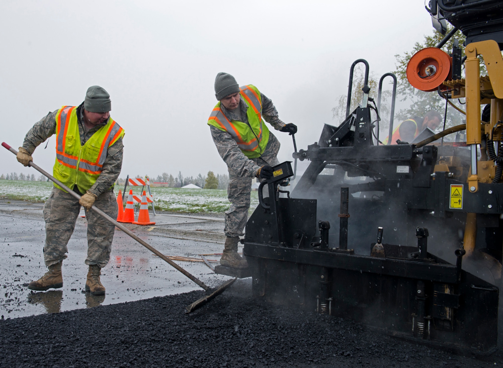 Senior Airman Eric Lippold (left) and Airman 1st Class Cody Vanwinkle, both heavy equipment operators from the 773d Civil Engineer Squadron, lay down pavement near the People's Center on Joint Base Elmendorf-Richardson, Sept. 23, 2013. Despite the early snowfall, the 773 CES was out working to repair this road. (U.S. Air Force photo/Staff Sgt. Zachary Wolf)