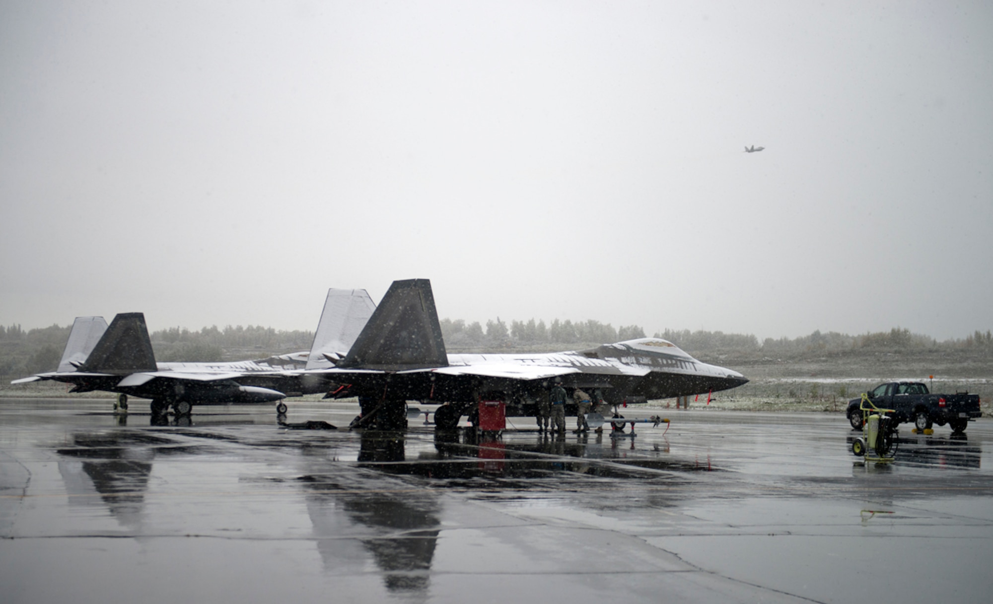 A F-22A Raptor flies over a maintenance crew made up of active-duty and reserve Airmen from Joint Base Elmendorf-Richardson, Sept. 23, 2013. The maintanence members were out in the early snowfall ensuring the jets were ready to fly. (U.S. Air Force photo/Staff Sgt. Zachary Wolf)