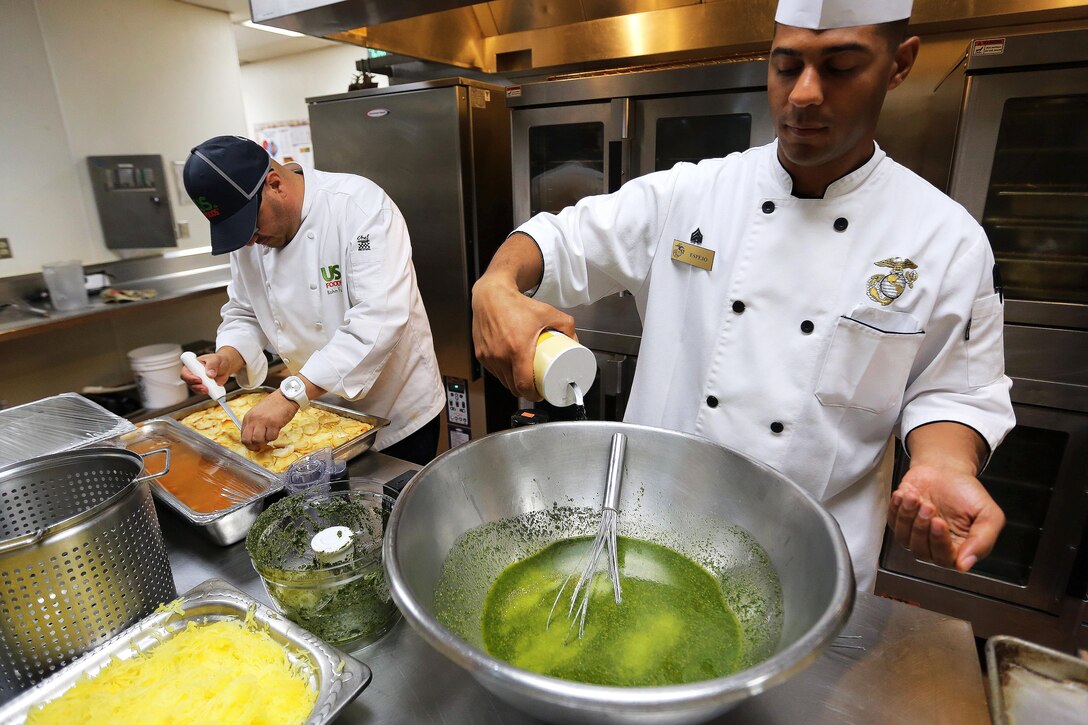 Chef Rahm Fama, left, and Sgt. Michael Espejo prepare lunch for Marines at the 14-Area Chow Hall here on Sept. 25. Fama is a guest chef at the chow hall and taught Marines how to make several dishes from a new book he will be publishing and give them tips to "spice up" their culinary skills. Fama is a Food Network chef and the corporate chef for US. Foods. Espejo is a food specialist Marine for Combat Logistics Regiment 17.