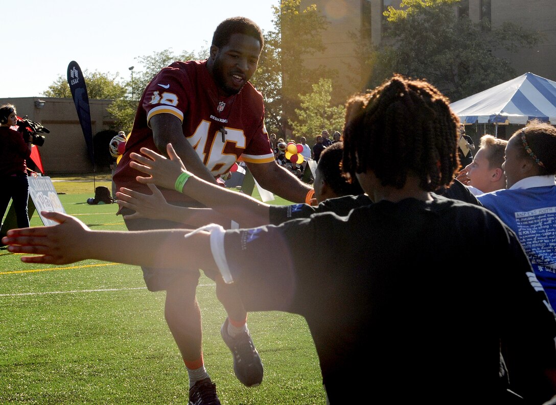 Washington Redskins running back Alford Morris high-fives children as he is introduced during the Salute to Play 60 Military Challenge at Joint Base Andrews, Md., Sept. 24, 2013. During the challenge, Redskins players and celebrity trainers lead the children through stations that included passing drills, agility ladders, 40-yard dash and a lesson on health eating habits. (U.S. Air Force photo/ Airman 1st Class Nesha Humes)
